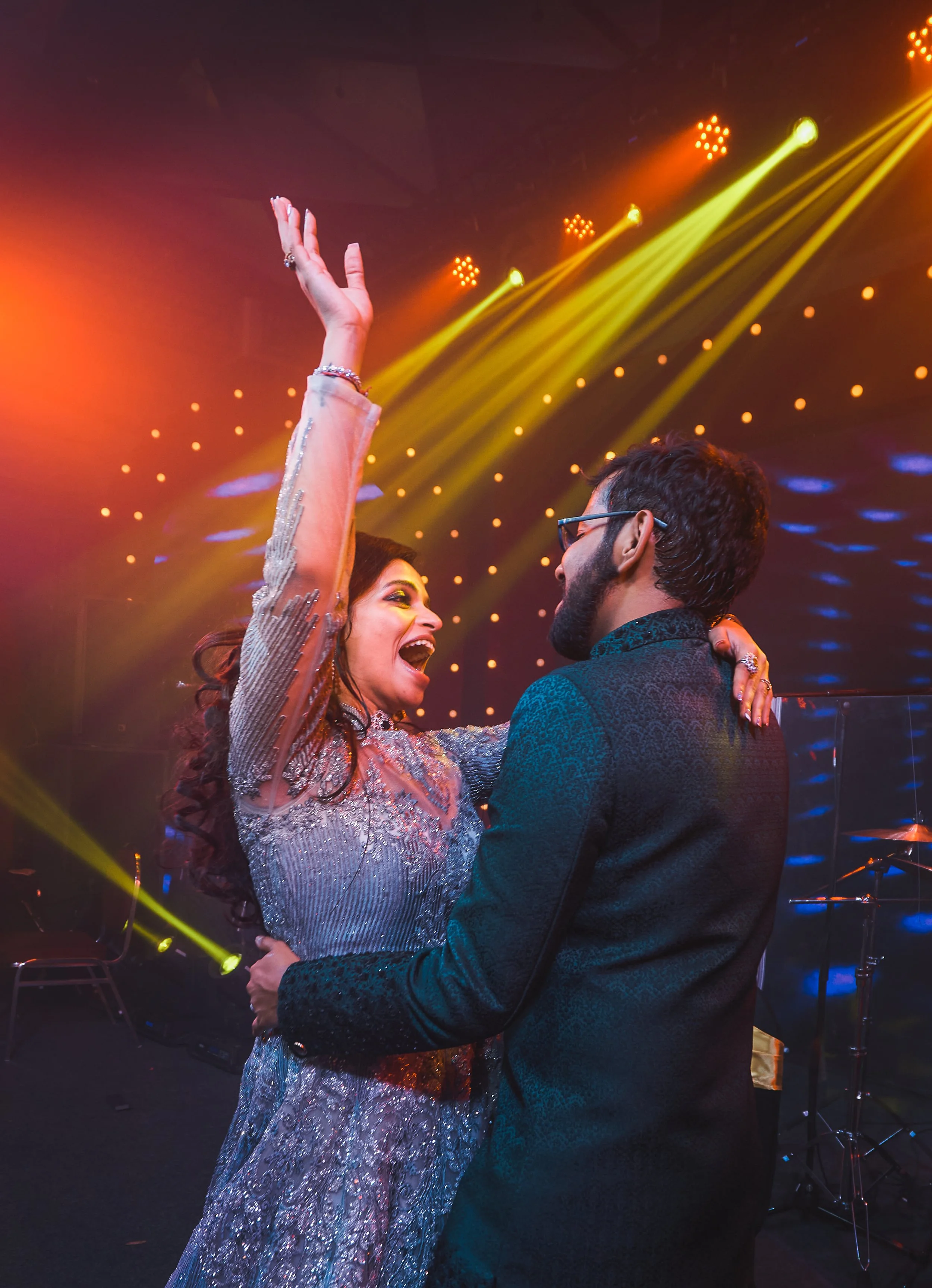 A woman and man dancing at a party with colorful stage lights and a dark background.