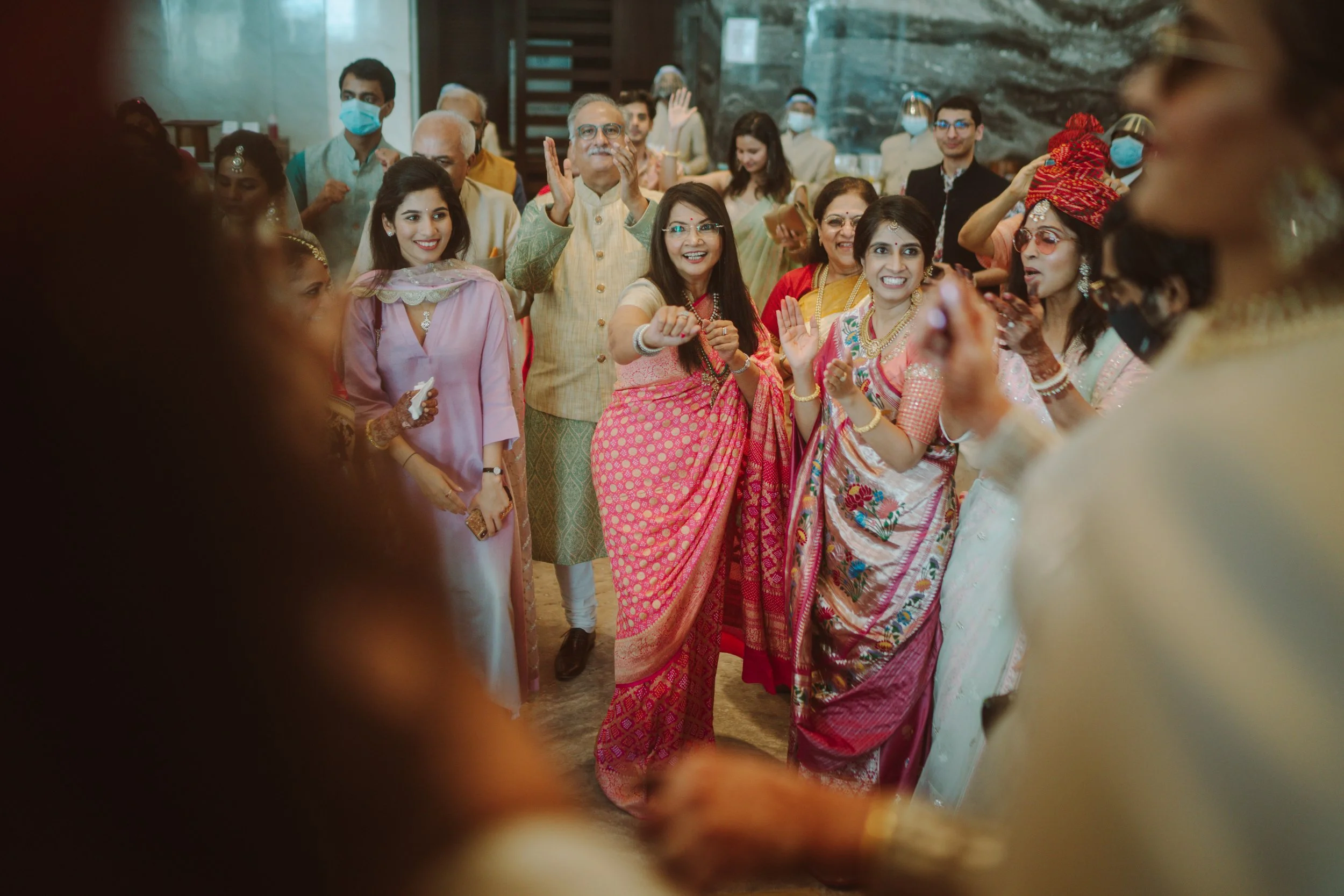 Group of people celebrating at a traditional Indian ceremony, all dressed in colorful sarees and kurtas, smiling and looking joyful.