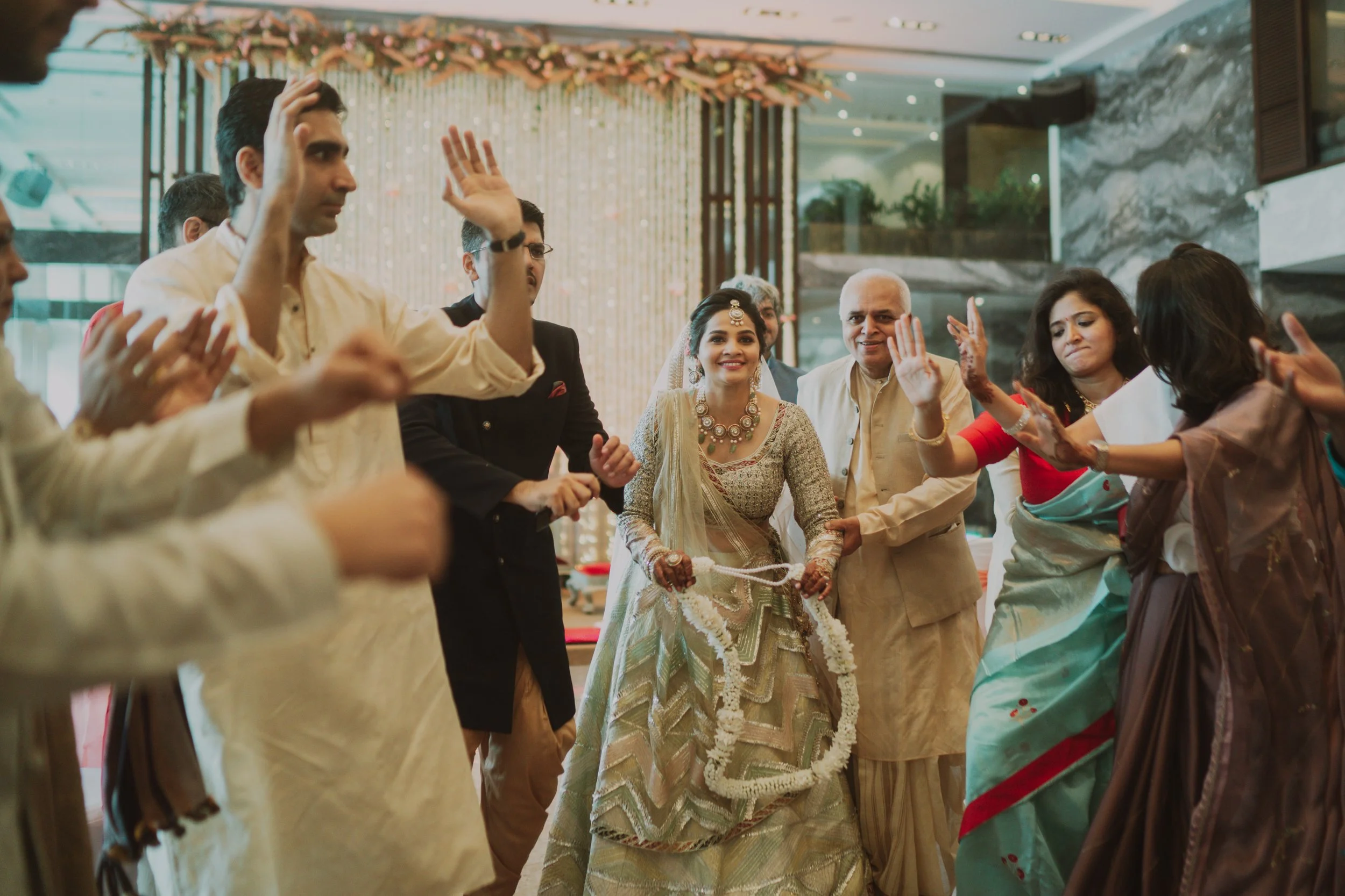A traditional Indian wedding celebration with a bride in ornate attire and jewelry, surrounded by family and friends performing a ceremonial dance or ritual indoors.
