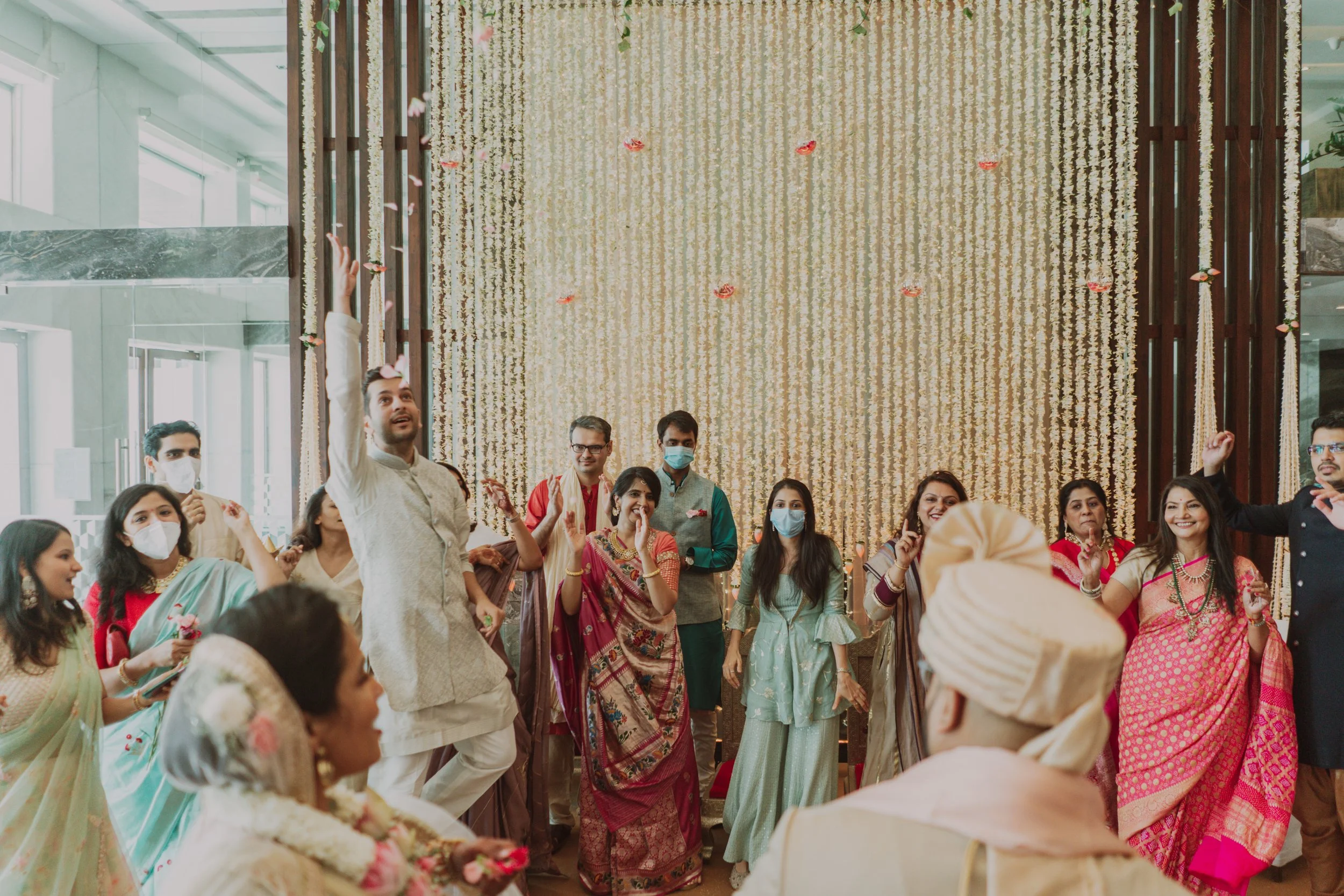 A group of people dressed in traditional Indian attire gathered at a celebration with floral decorations and gold backdrop arches.