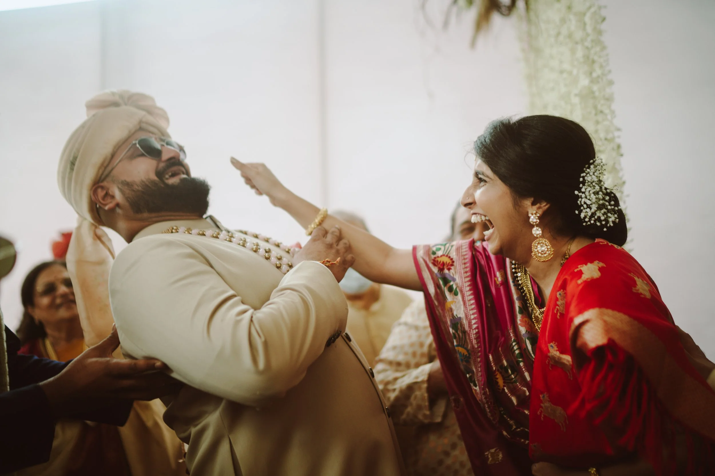 A joyful woman in traditional Indian attire playfully interacts with a man dressed in cultural Indian clothing, both smiling widely during a celebration.