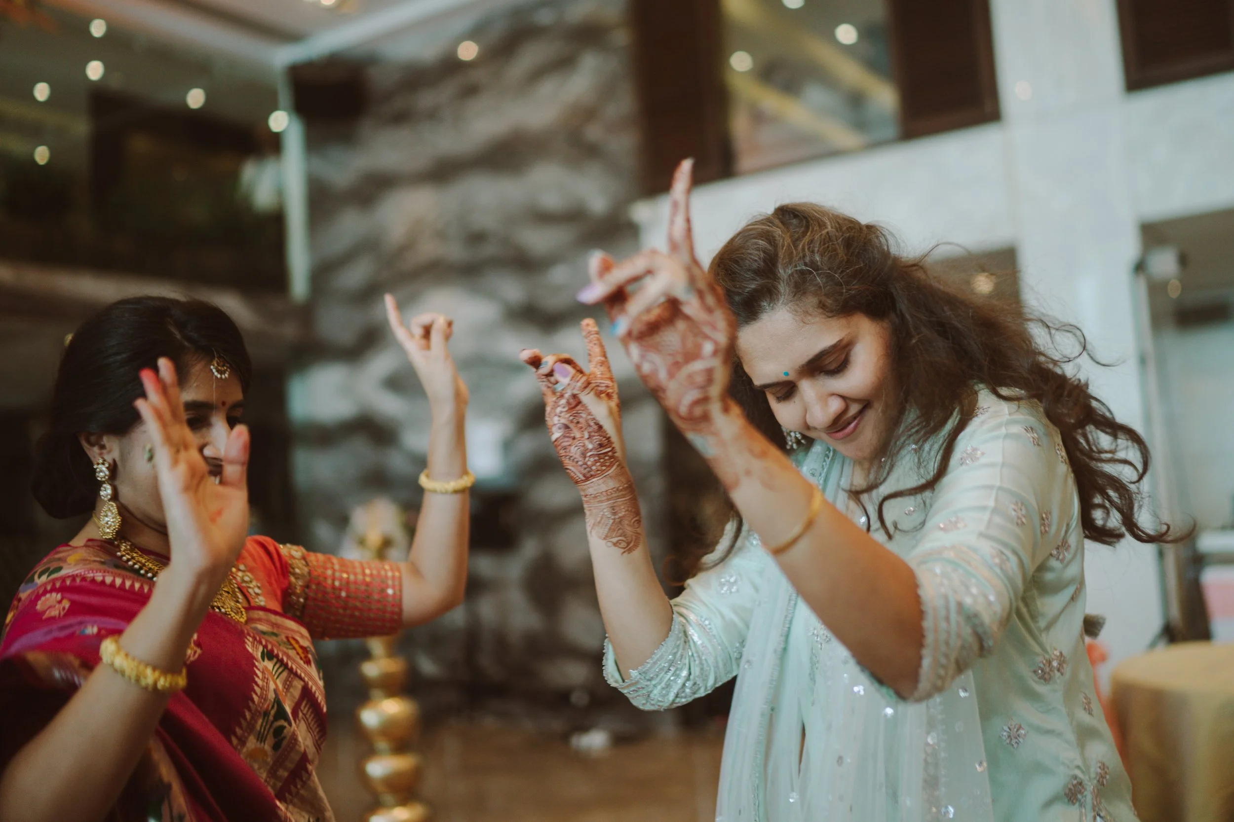 Women celebrating at a traditional Indian wedding, dancing and smiling, wearing colorful sarees and jewelry.