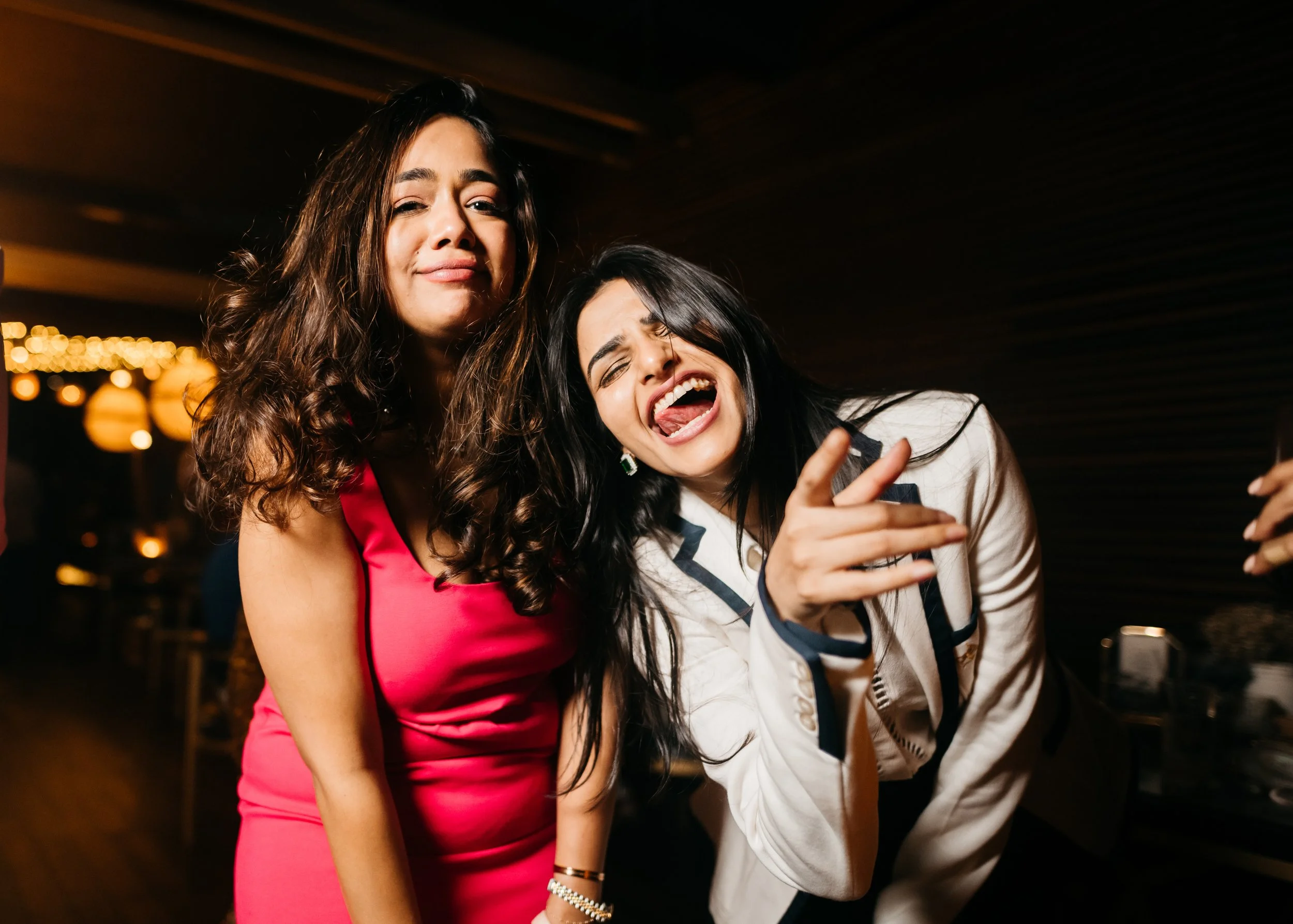 Two women enjoying a lively conversation at an indoor social gathering, with warm lighting and blurred background.