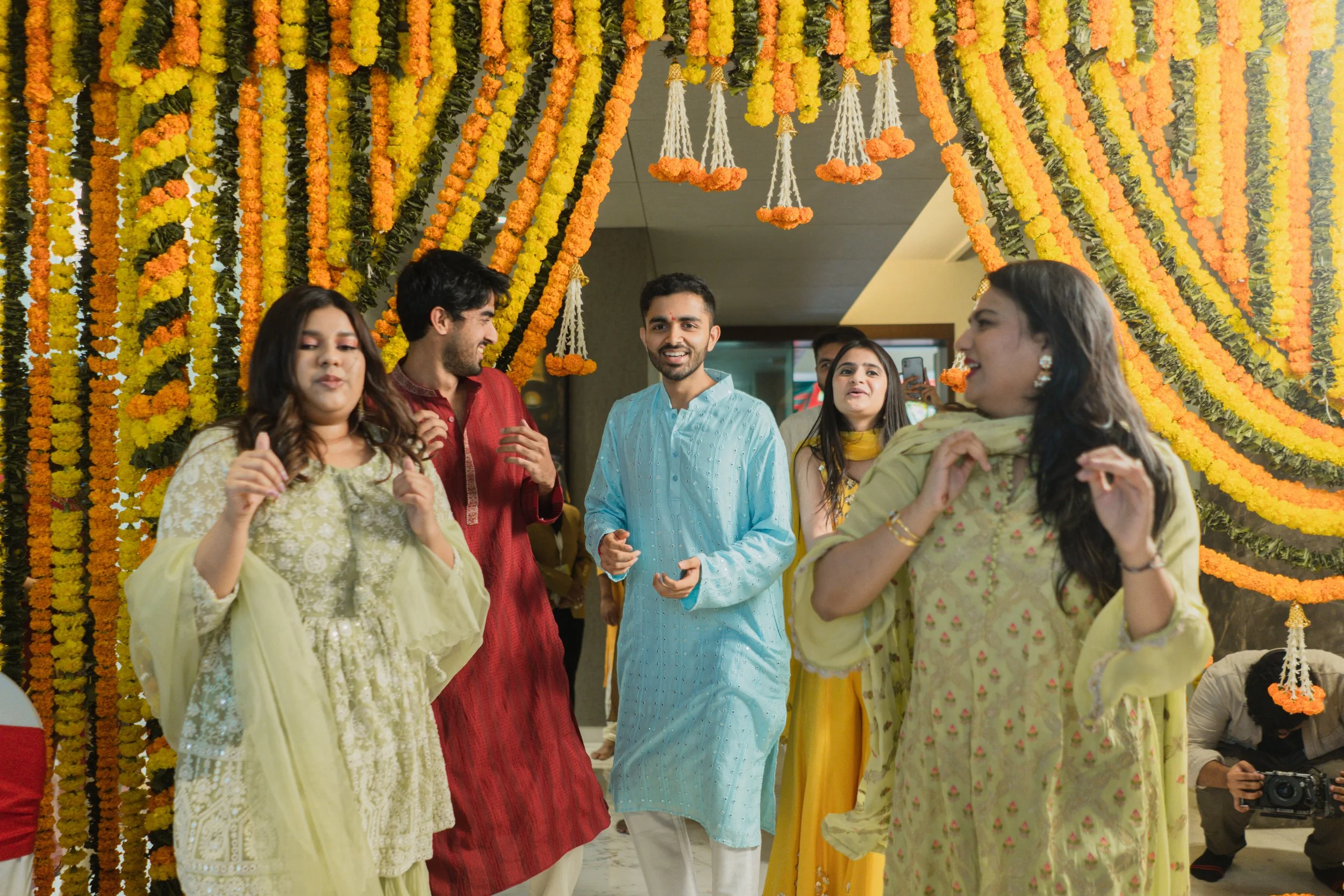 People dancing and celebrating at a wedding or festive event decorated with yellow and orange marigold flower garlands.
