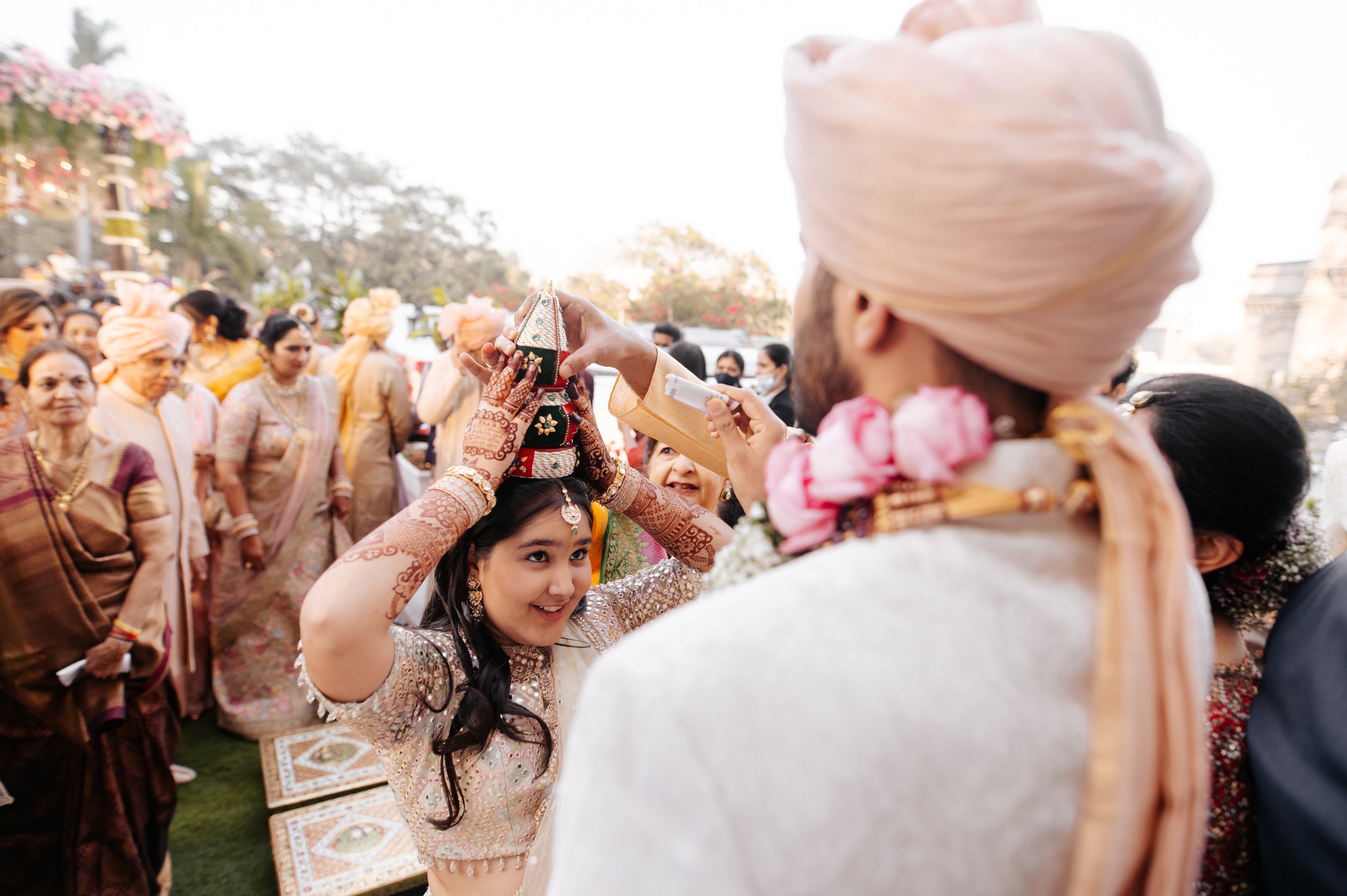Young woman participating in a traditional Indian wedding ceremony, placing a decorative crown on an elderly man's head, surrounded by family and friends dressed in colorful, traditional attire.