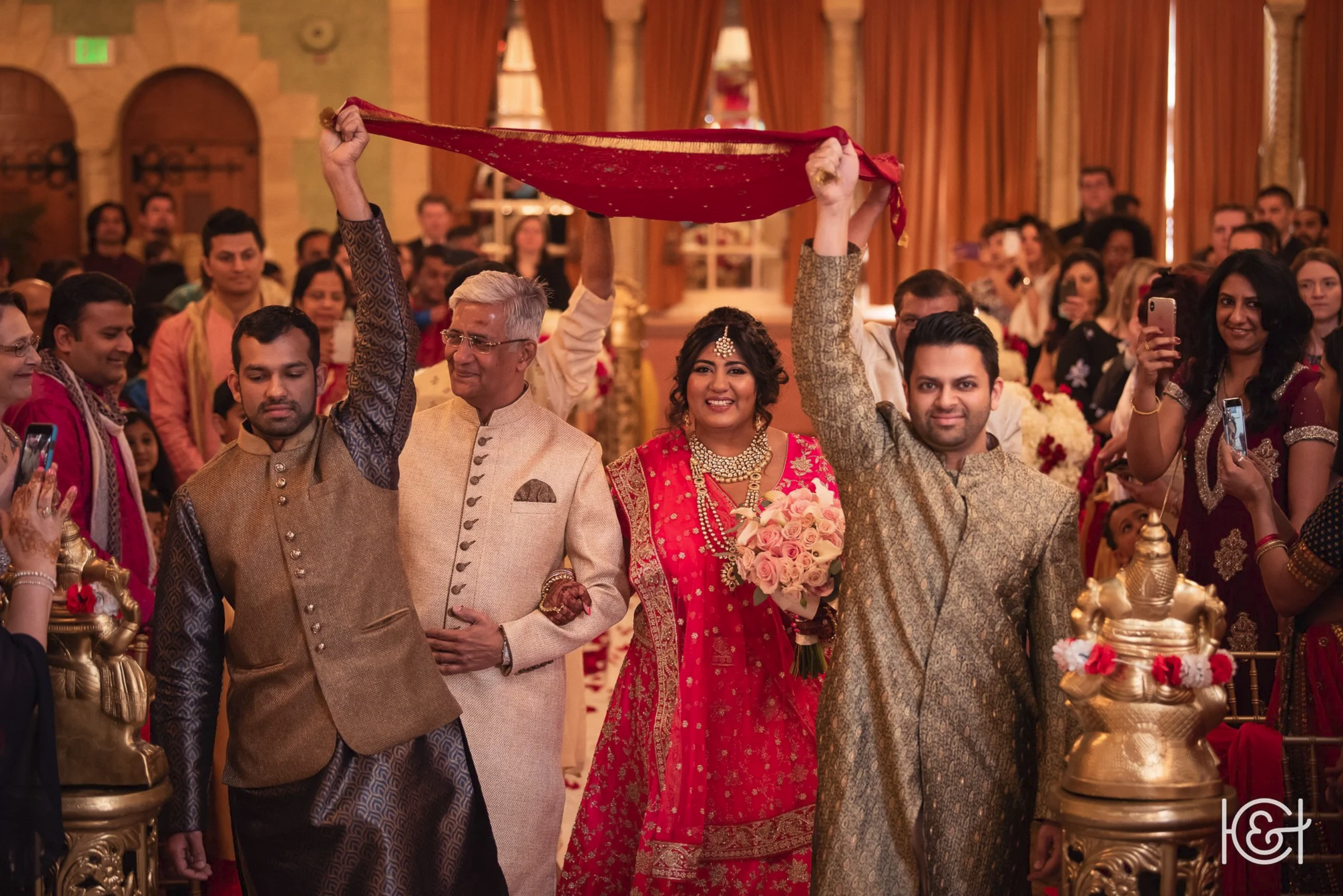 Indian wedding ceremony with bride and groom in traditional attire, surrounded by family and friends, indoors with ornate decor.