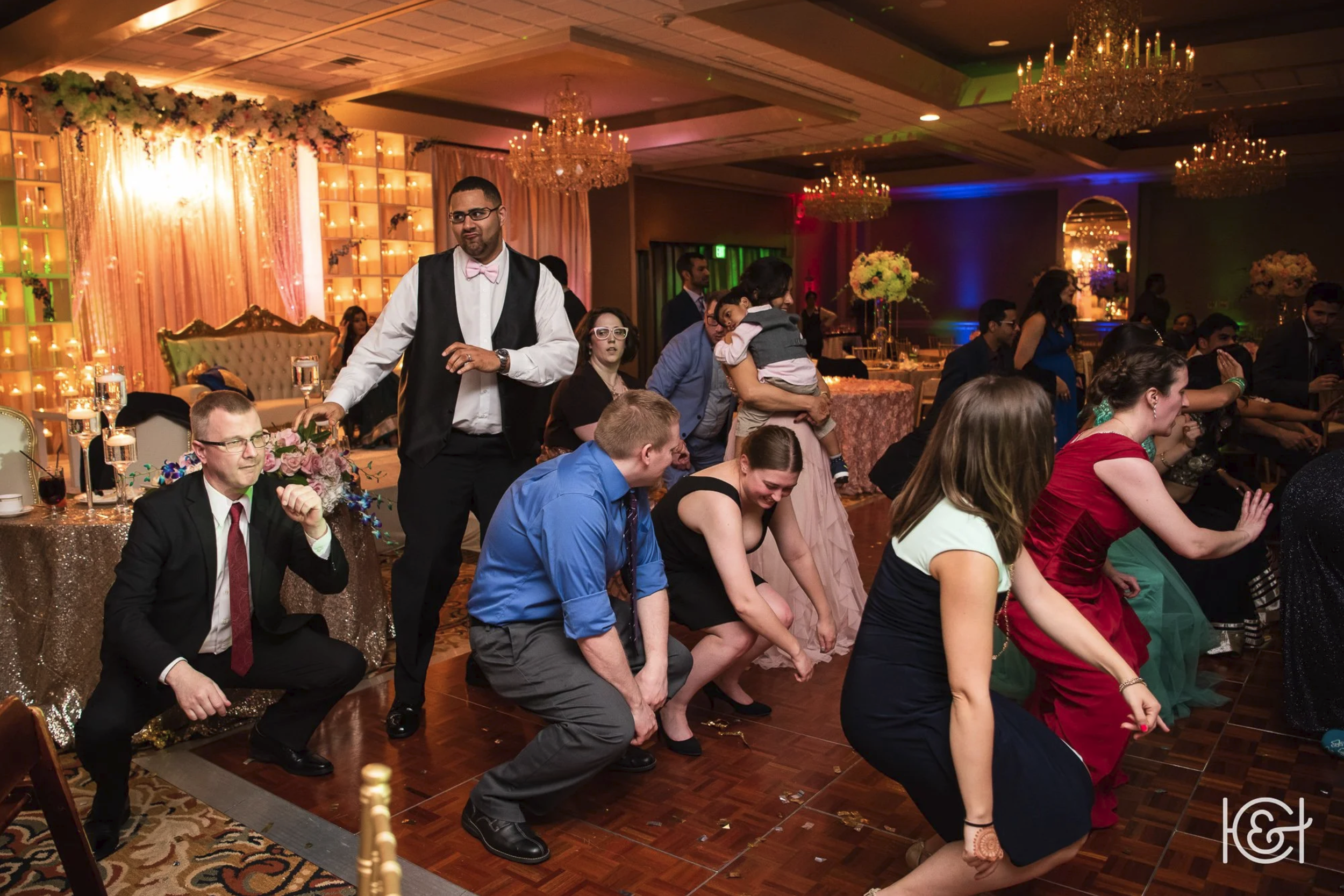 People dancing at a wedding reception with chandeliers, floral decorations, and elegant table settings.