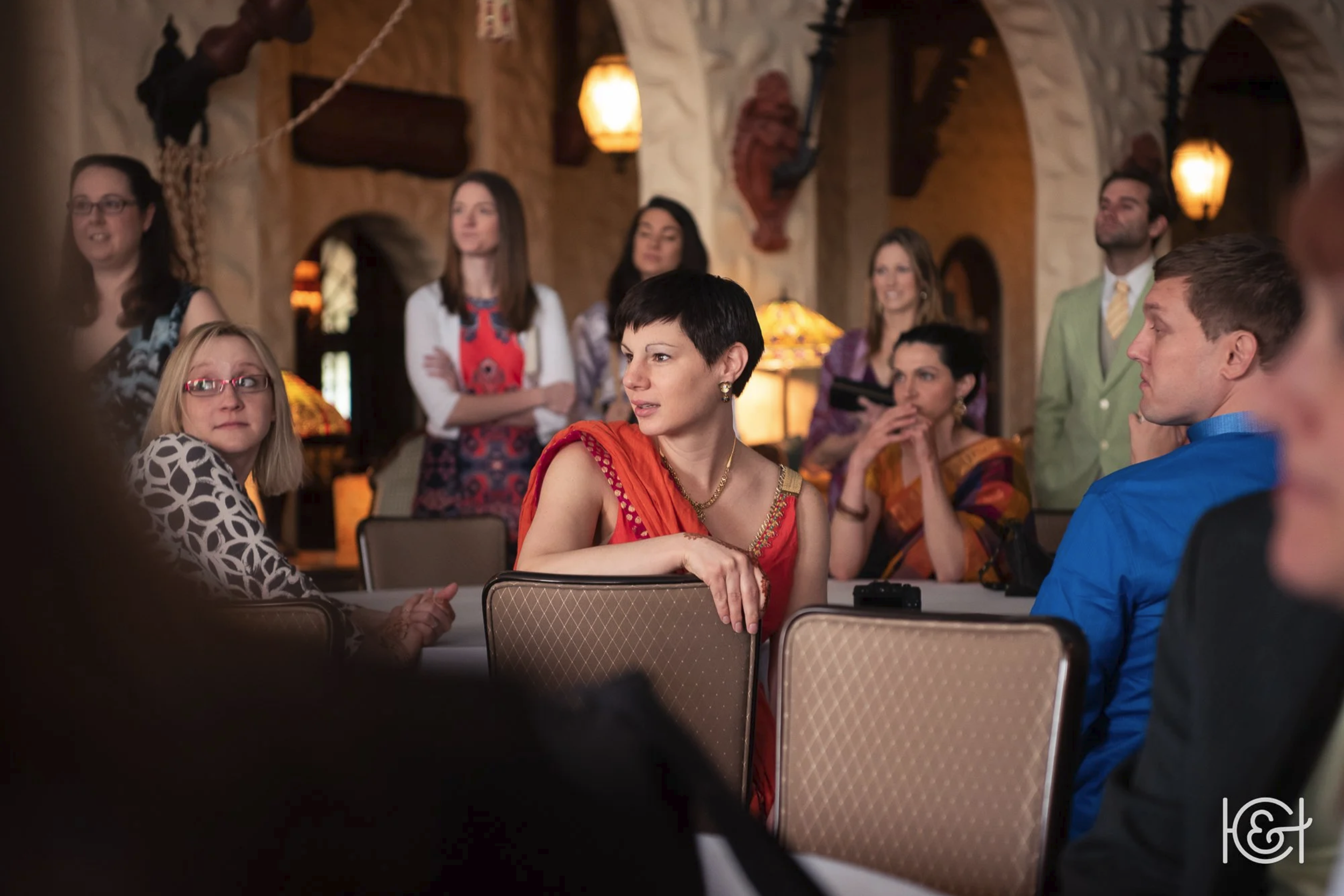 Group of people in a cozy, rustic room with warm lighting, sitting and standing, appearing to listen to or participate in a discussion or presentation.