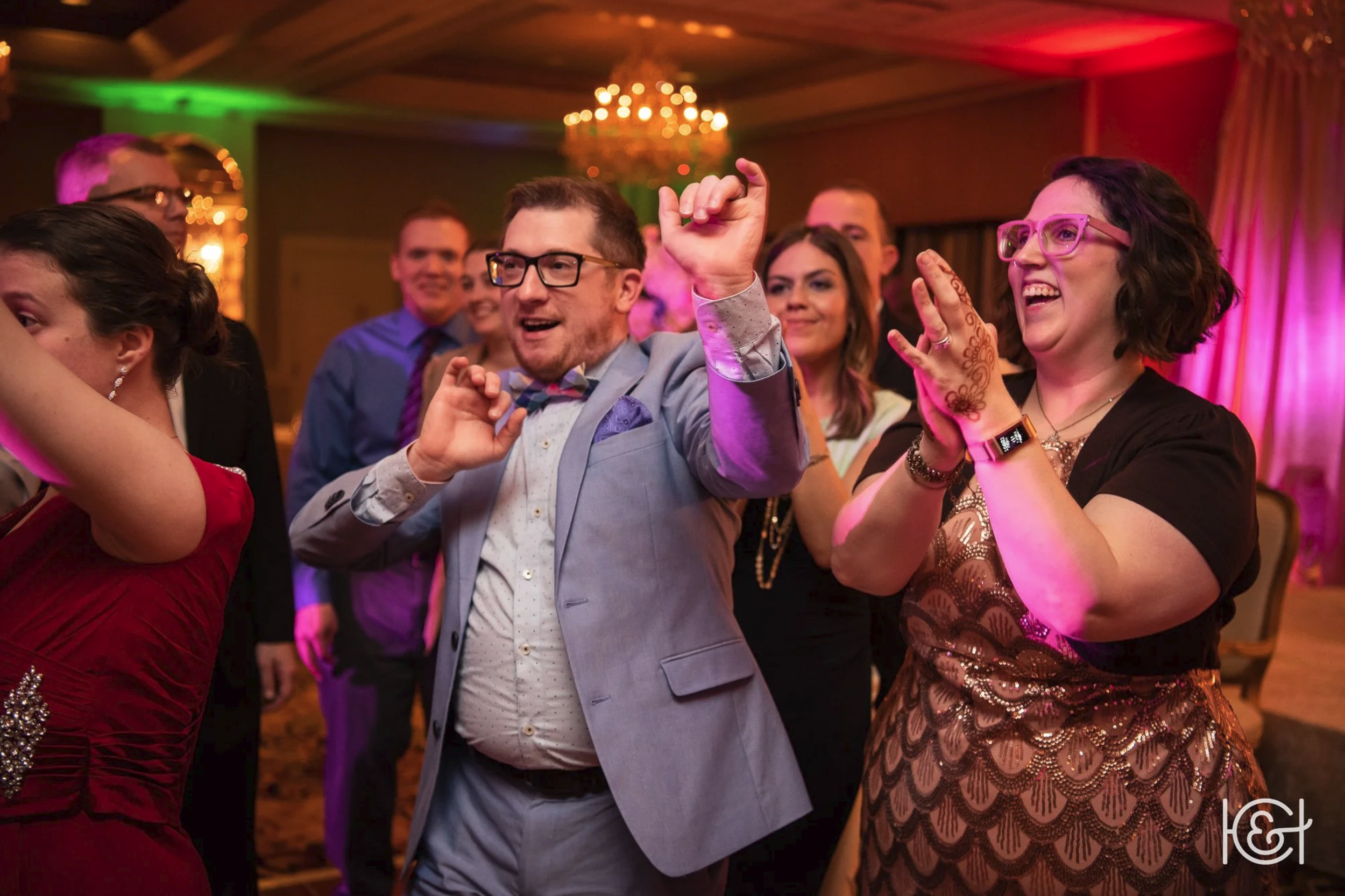People dancing and celebrating at a party or wedding reception in a decorated venue with colorful lighting.