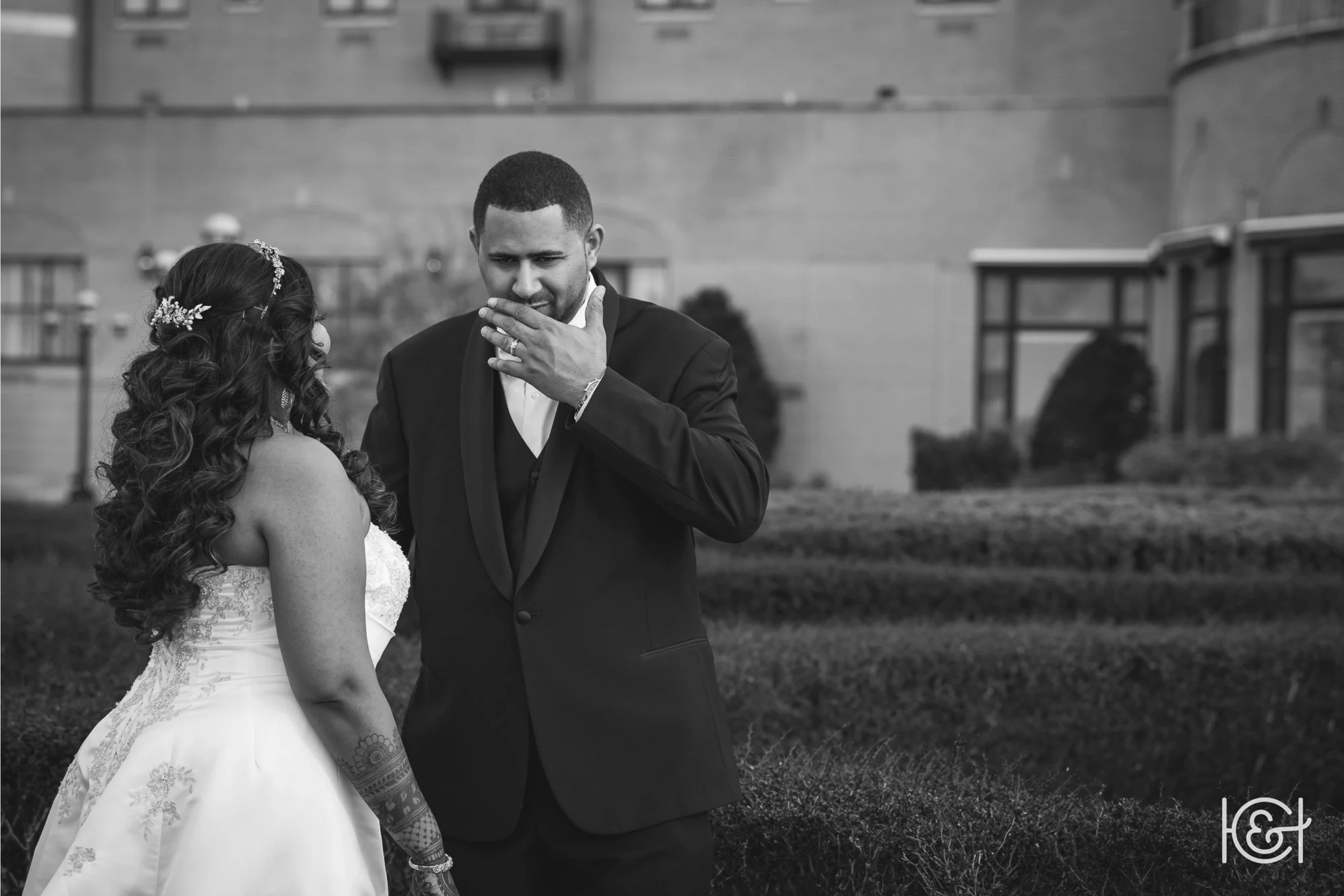 A wedding couple sharing a moment outdoors, with the groom touching his face and the bride looking at him.