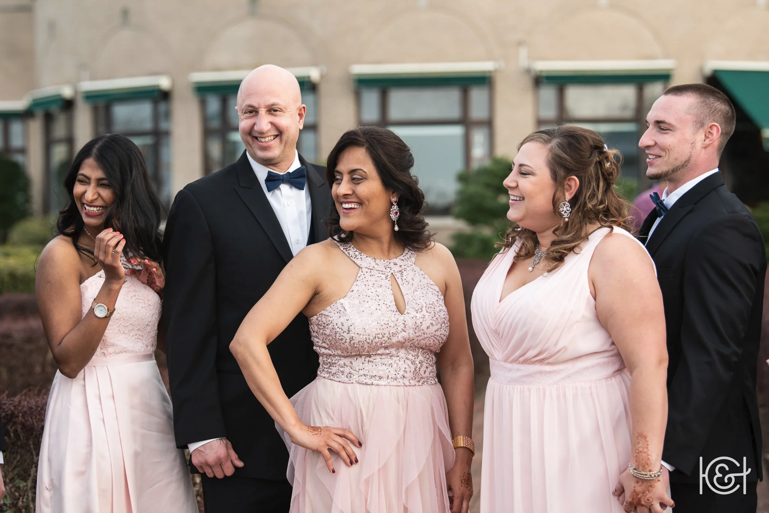 Group of five adults dressed in formal attire, smiling outdoors during daytime