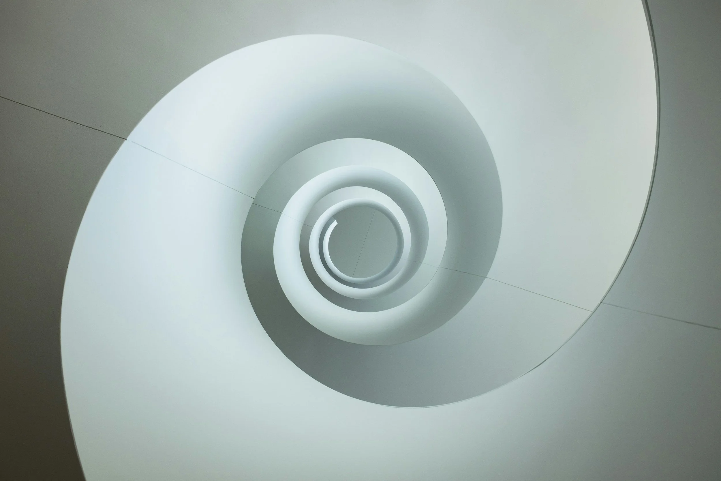 Interior view of a modern, spiral white staircase with circular light fixtures, seen from below.