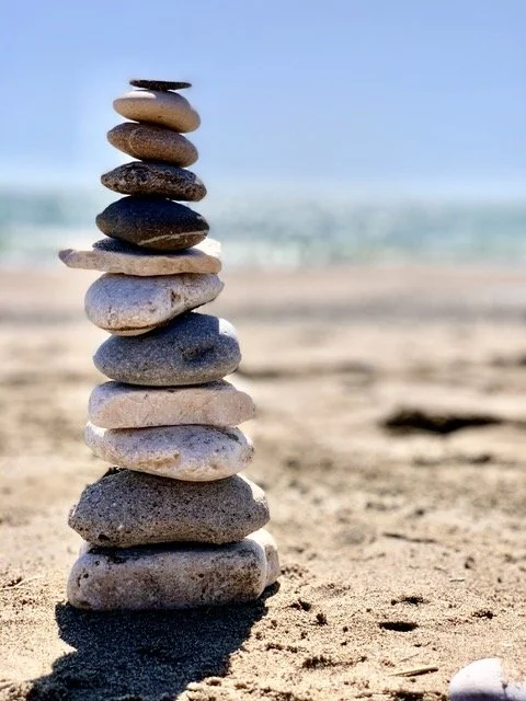 Stacked stones on a sandy beach with ocean and sky in the background.