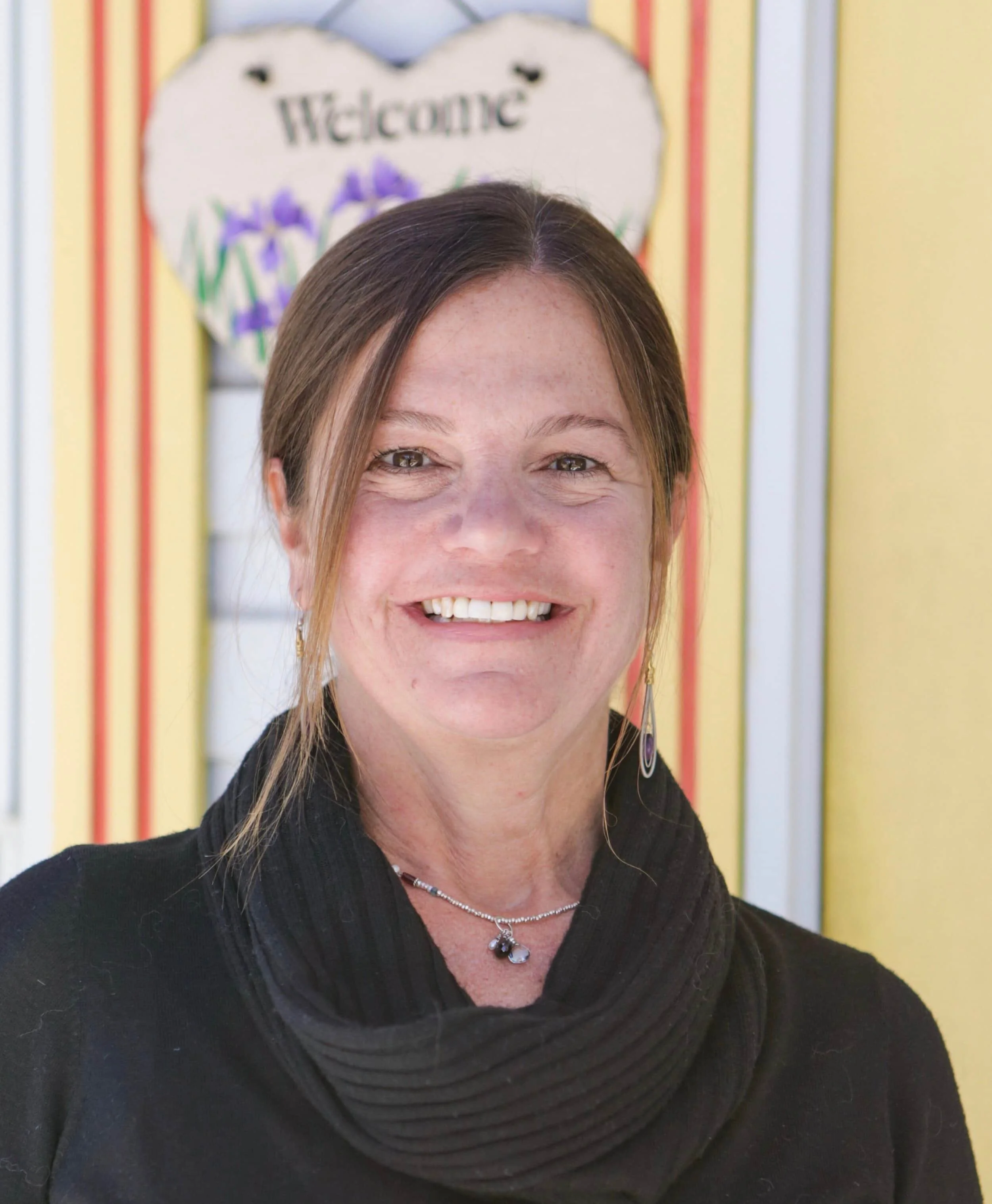 A woman smiling in front of a colorful background with a welcome sign.