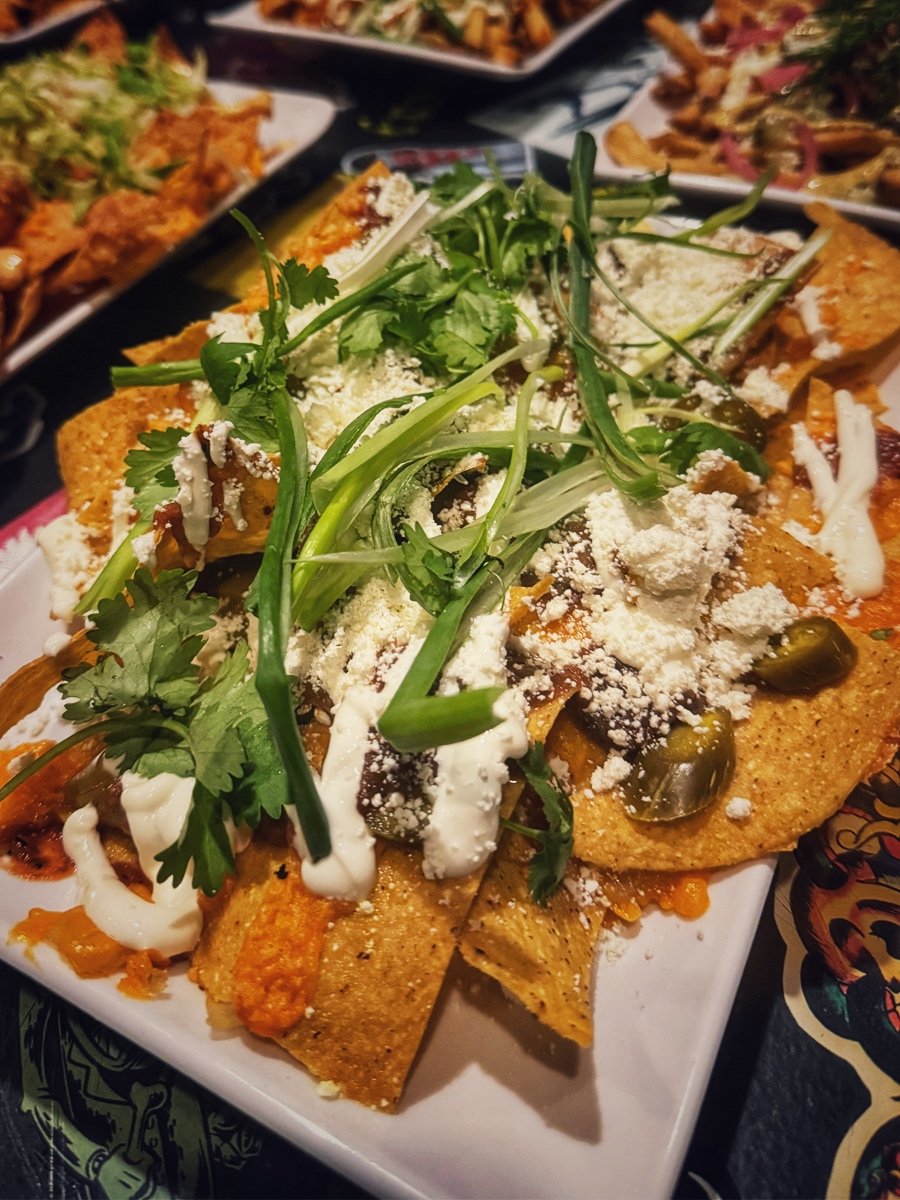 Plate of nachos topped with shredded cheese, sour cream, chopped cilantro, sliced jalapeños, and green onions.