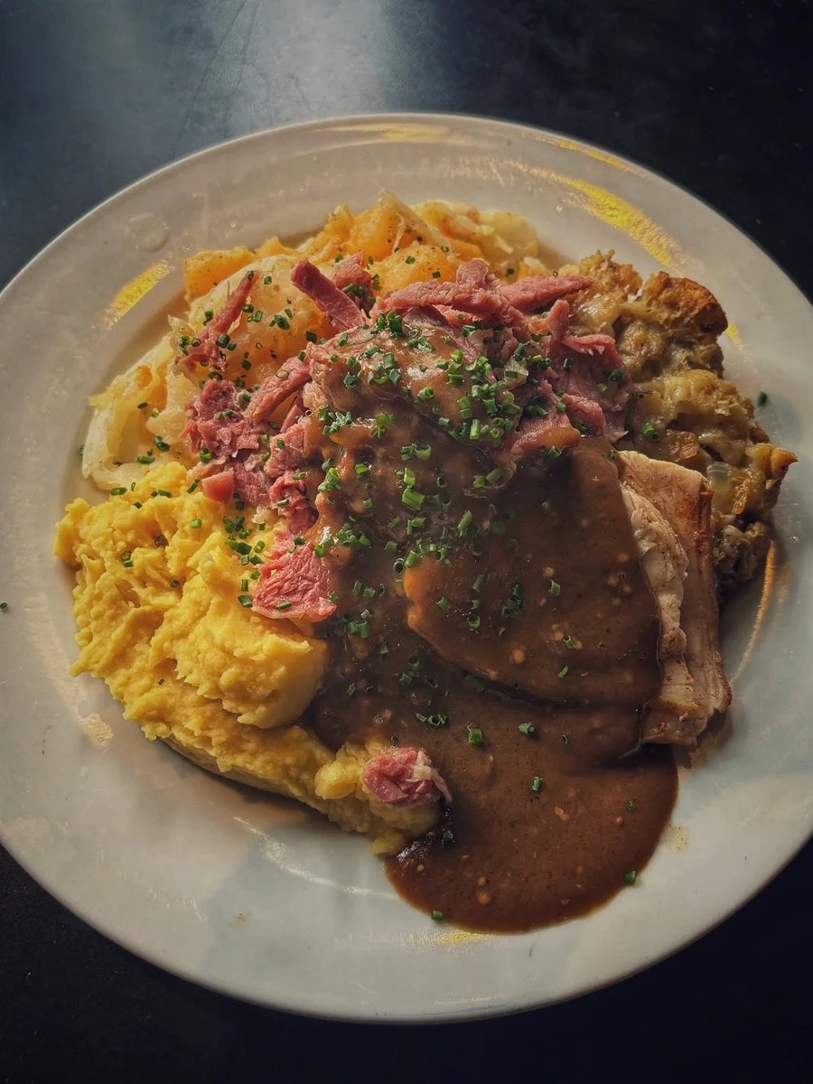 Plate of mashed potatoes topped with chopped chives, mashed potatoes, sliced cooked ham, and a pork chop with brown gravy, garnished with additional chopped chives.