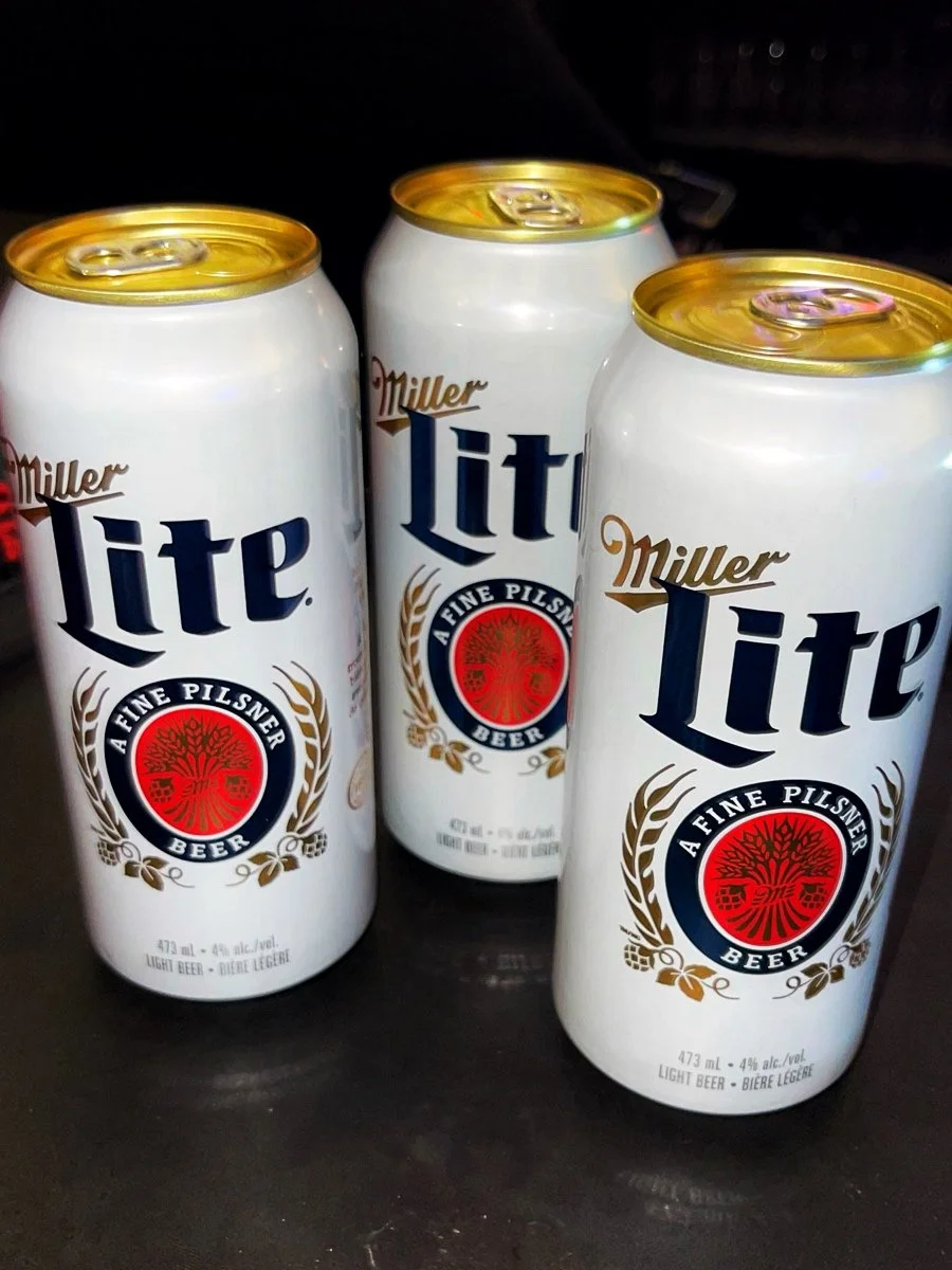 Three cans of Miller Lite light beer on a dark surface.