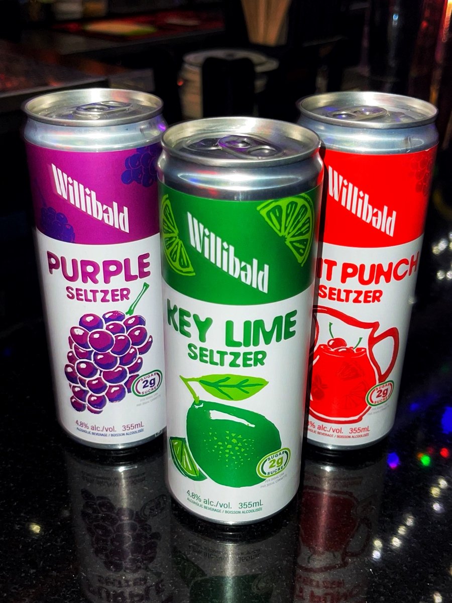 Three cans of Wiliberal flavored seltzers on a black surface. The purple can is Grape flavor, the green can is Key Lime flavor, and the red can is Fruit Punch flavor.