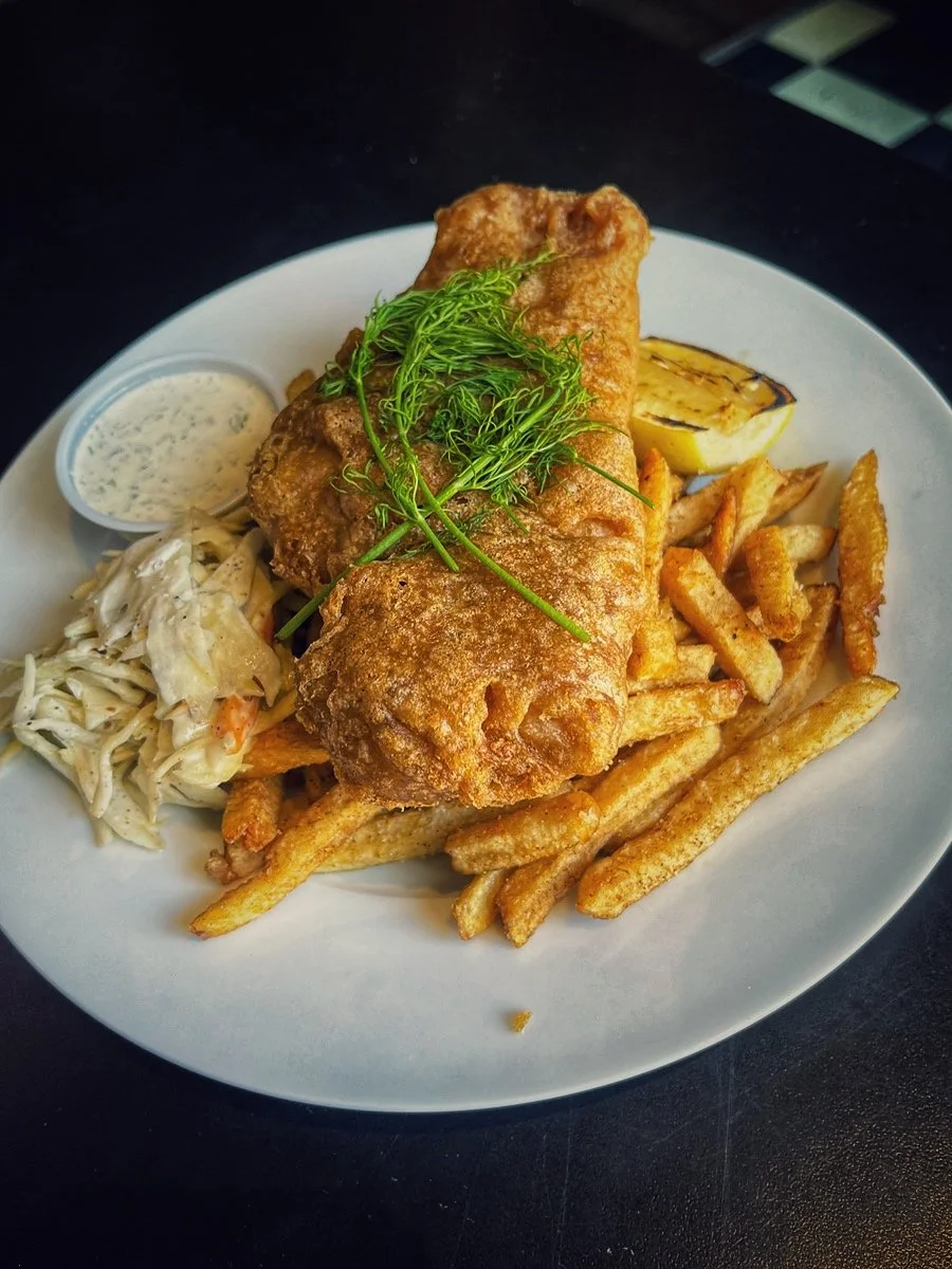 Fried fish fillet with French fries, coleslaw, grilled lemon, and tartar sauce on a white plate.