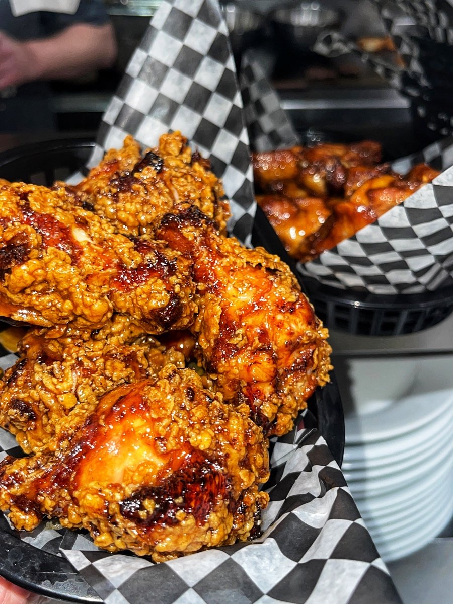 Close-up of hot honey flavoured fried chicken wings in a black basket lined with black and white checkered paper.