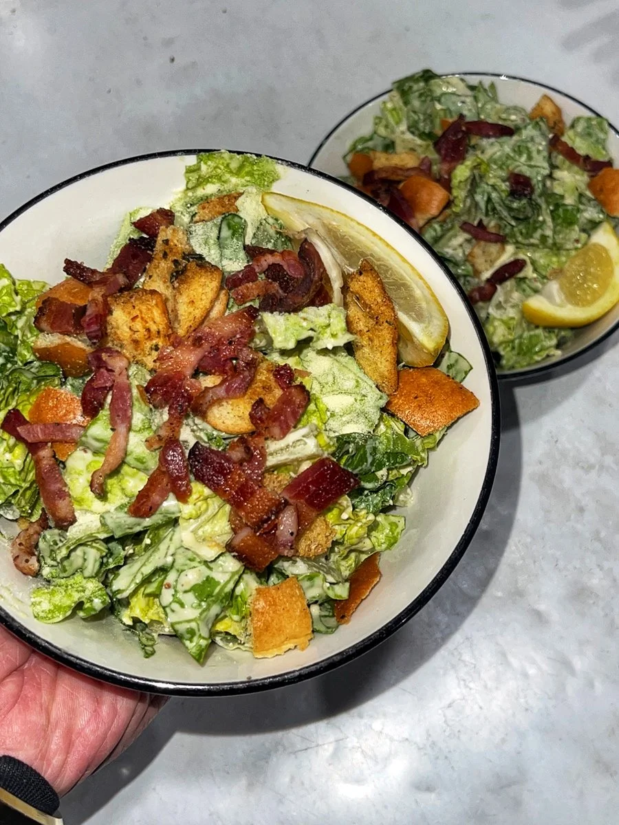 Two bowls of Caesar salad with lettuce, croutons, bacon bits, and a lemon wedge.