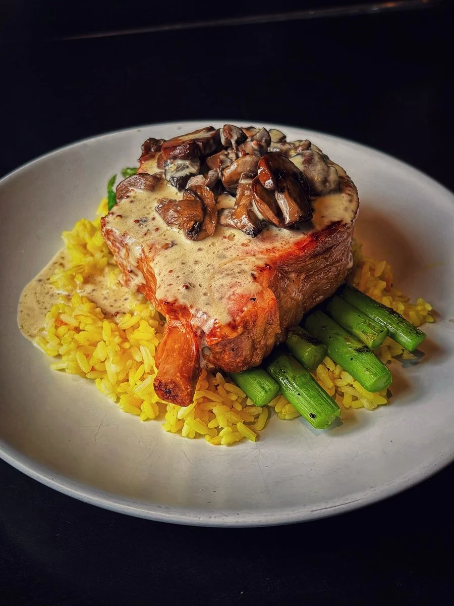 A plate of food featuring a pork chop with mushroom gravy on top, served over yellow rice with green asparagus spears.