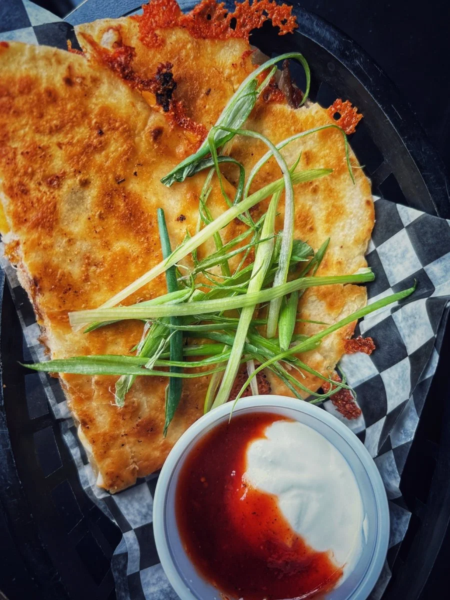 Quesadilla with green onions and a side of sour cream with hot sauce.