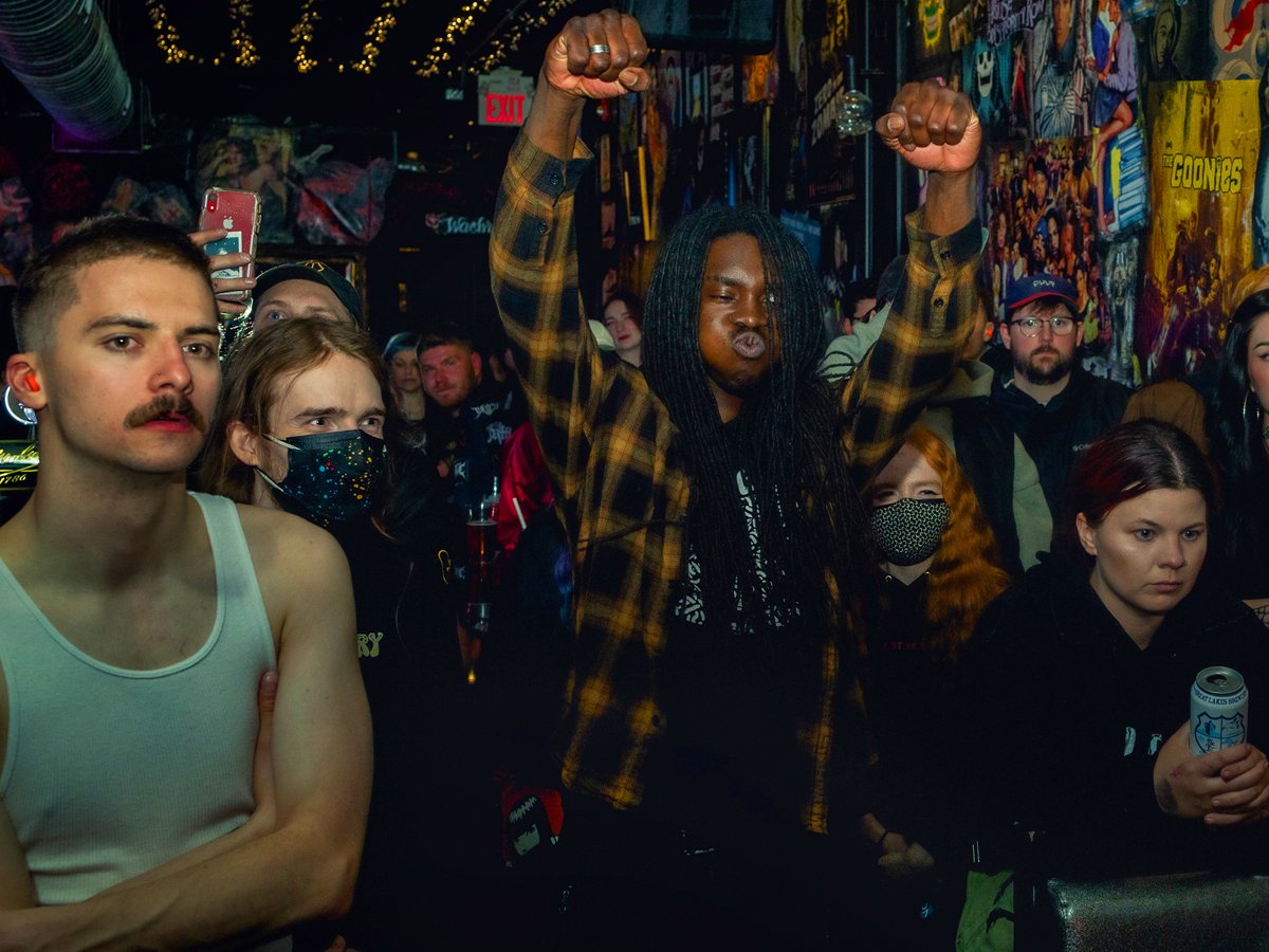 A diverse group of people at a concert or club inside a vibrant venue decorated with colorful murals and posters.