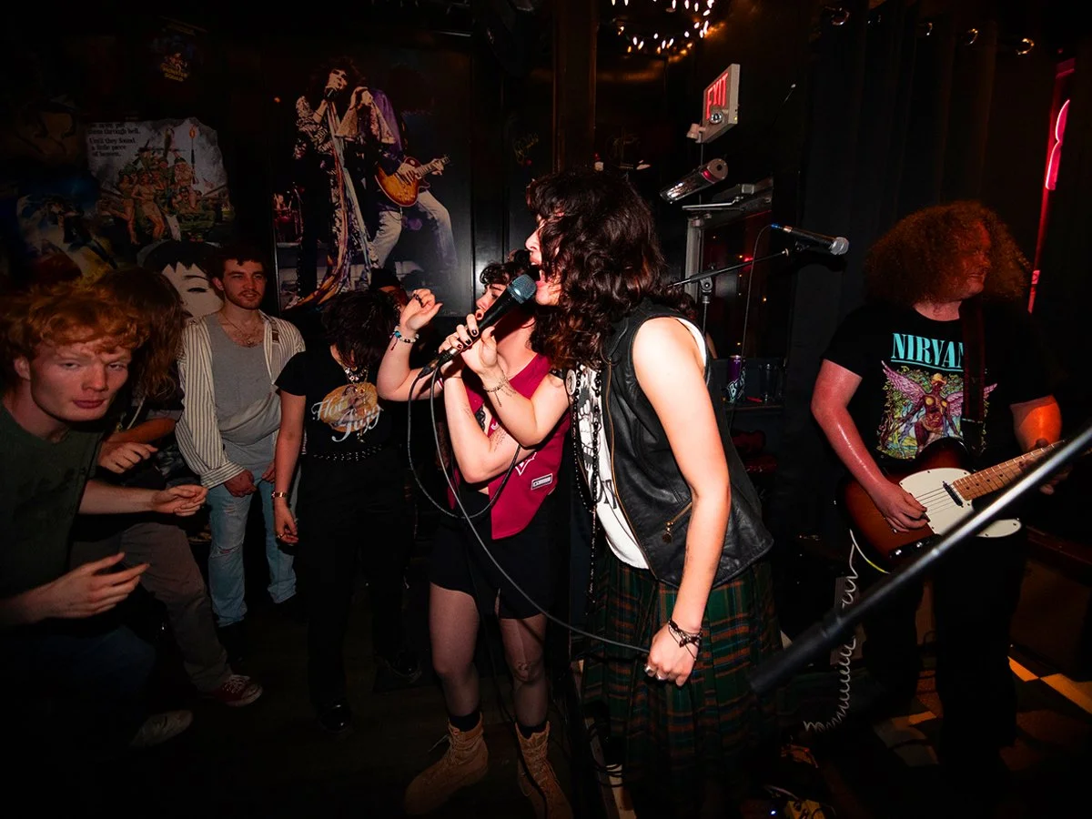 Women performing live music on stage with a guitarist and audience members watching.
