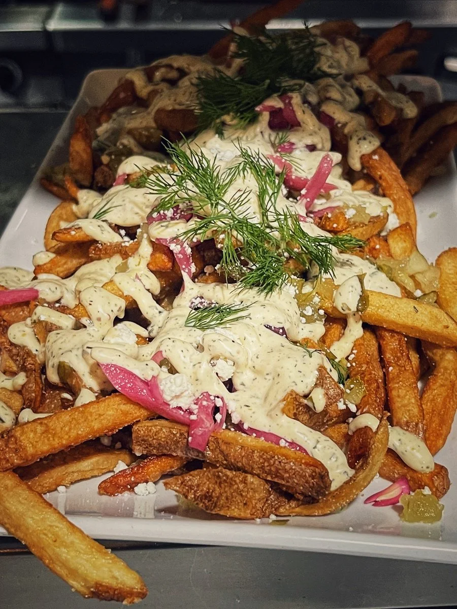 Plate of French fries topped with creamy sauce, pickles, red onions, and garnished with fresh dill.