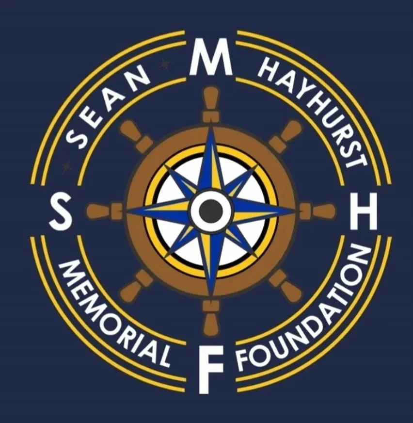 Logo of the Sean Hayhurst Memorial Foundation featuring a ship's wheel with a nautical compass at the center, set on a dark blue background.