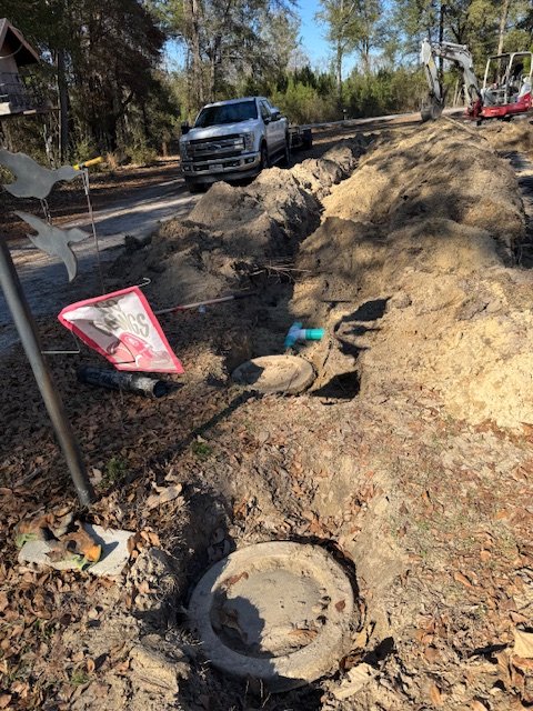 Construction site with excavation and a black pickup truck; orange and white construction equipment, and a broken traffic sign among dirt and debris.