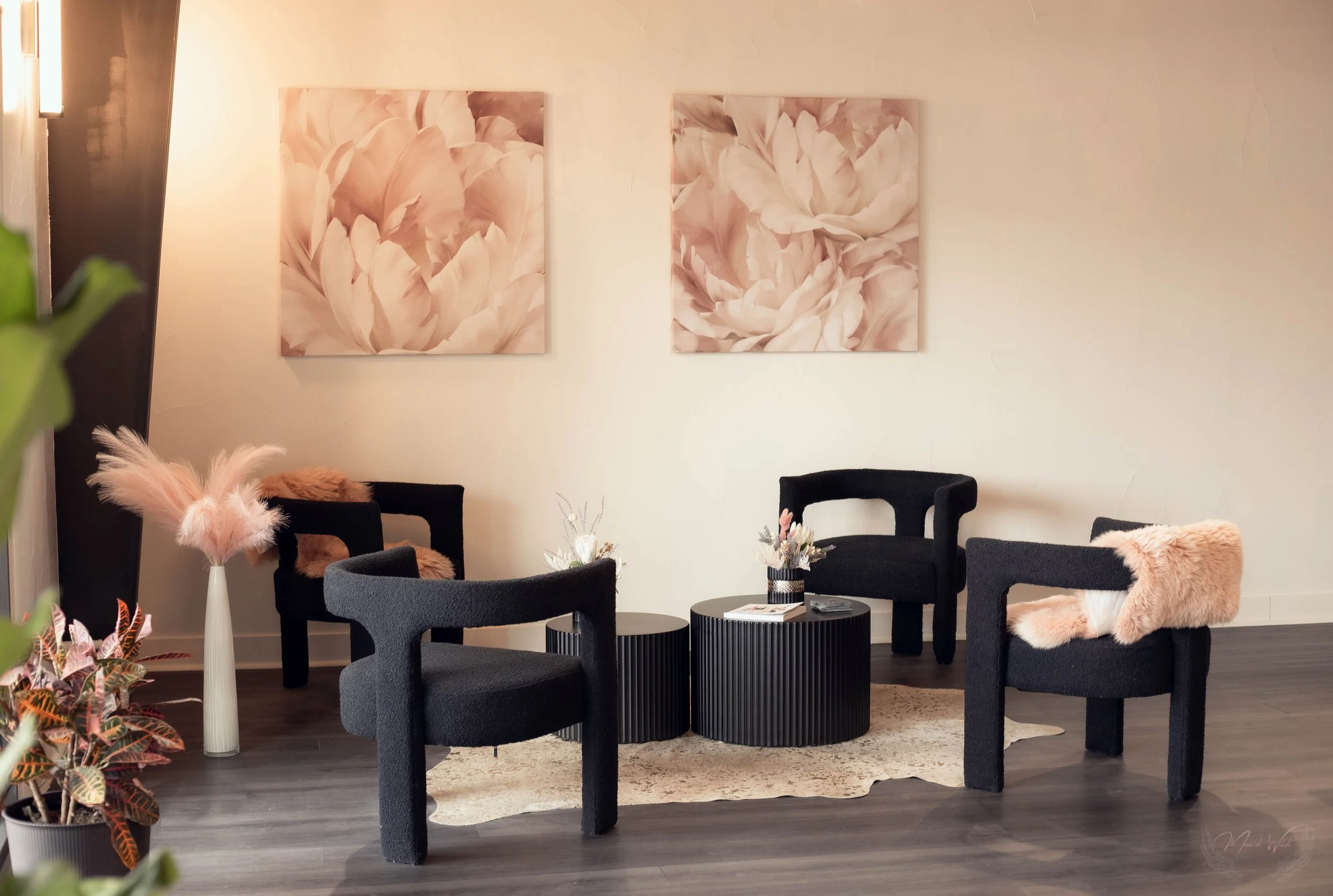 A modern sitting area with four black chairs, two round black coffee tables, a plant in the lower left corner, and light pink floral artwork on the wall.