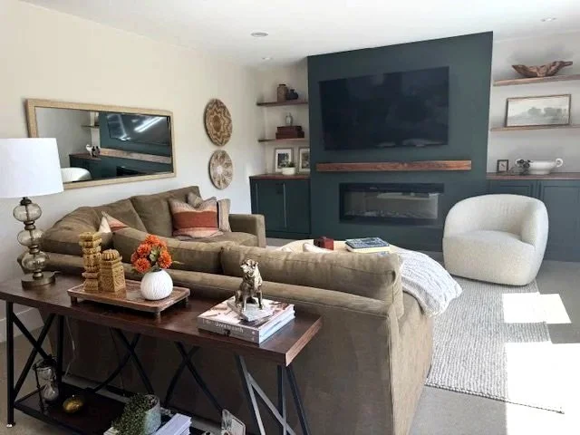 Living room with beige sofa, white armchair, fireplace, TV, mirror, shelves with decor, and various decorative items.