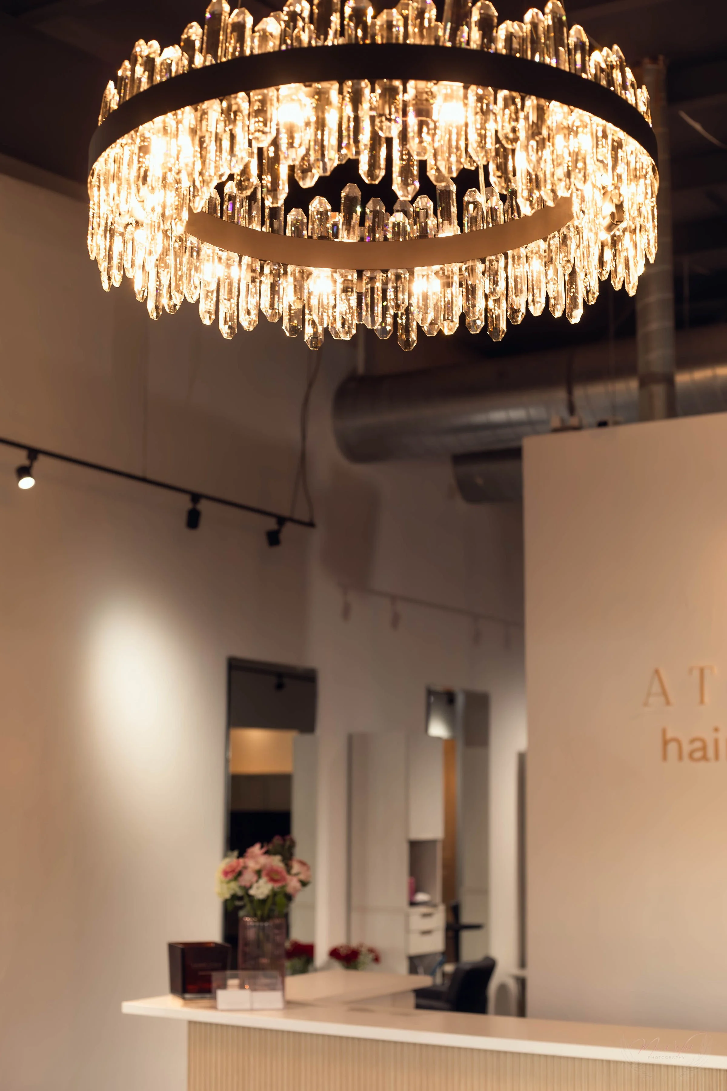 A bright crystal chandelier hanging from the ceiling in a modern interior hair salon space.