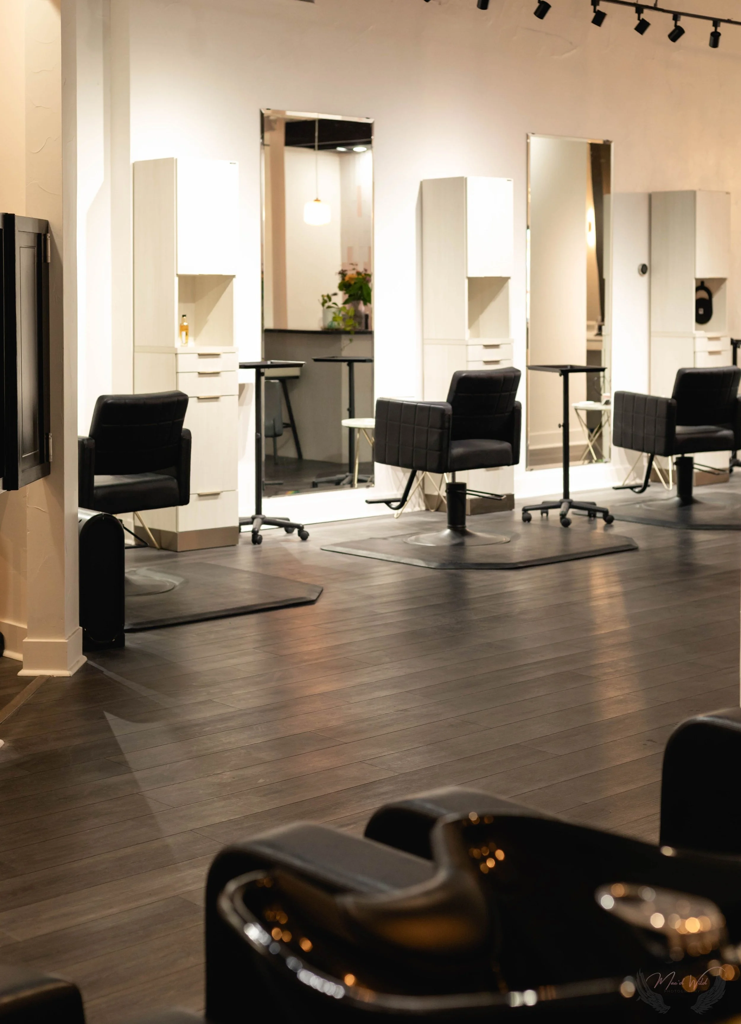 Empty hair salon with three styling stations, black chairs, mirrors, and hardwood floors.