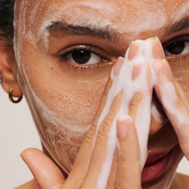 Person applying facial cleanser foam on face.
