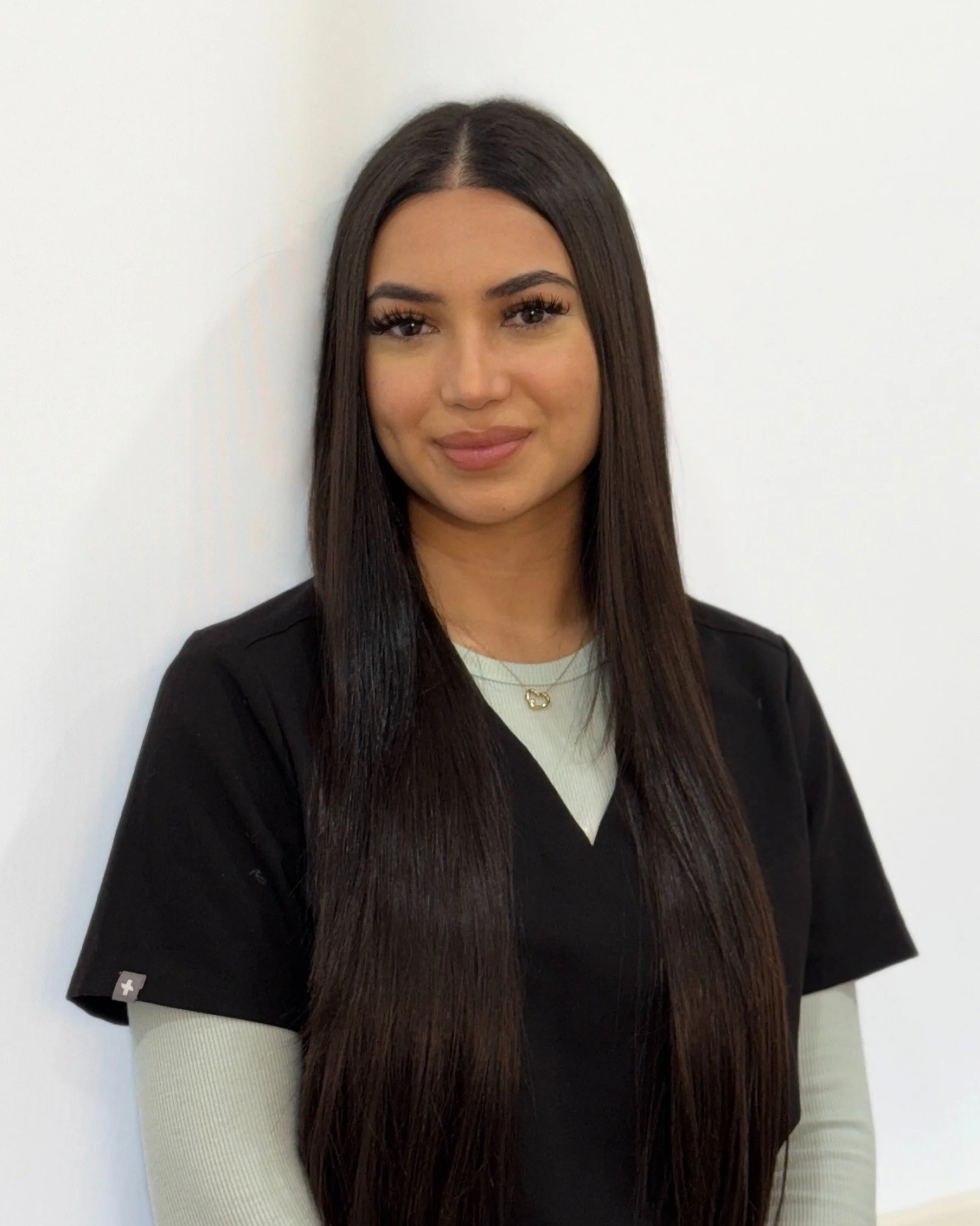 Woman with long dark hair wearing a black shirt, smiling against a plain background.