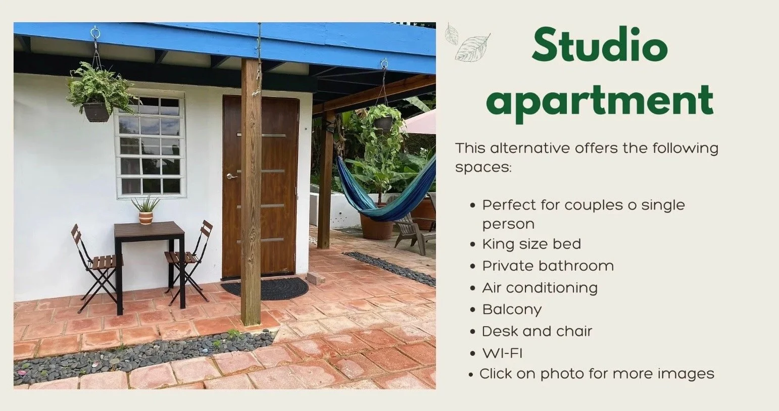 An outdoor studio apartment patio with terracotta tile flooring, a small wooden table with two folding chairs, a potted plant on the table, hanging plants, a hammock, and a wooden door next to a window, with a partial view of greenery and outdoor fur