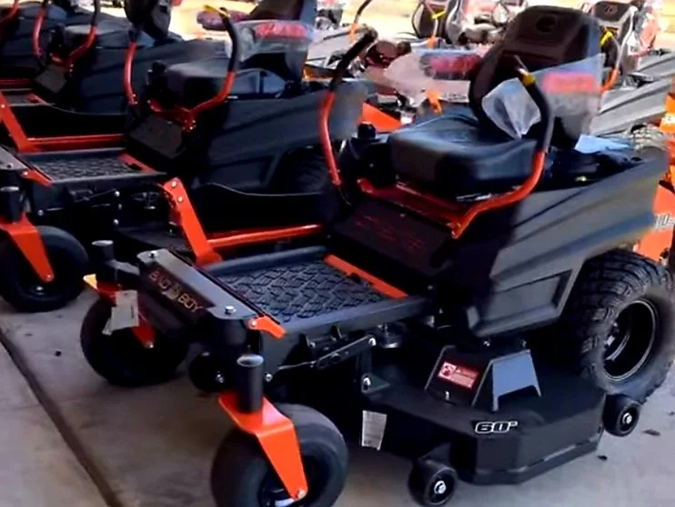 Multiple commercial ride-on lawn mowers or tractors with black and orange color schemes parked closely together in a store or warehouse.