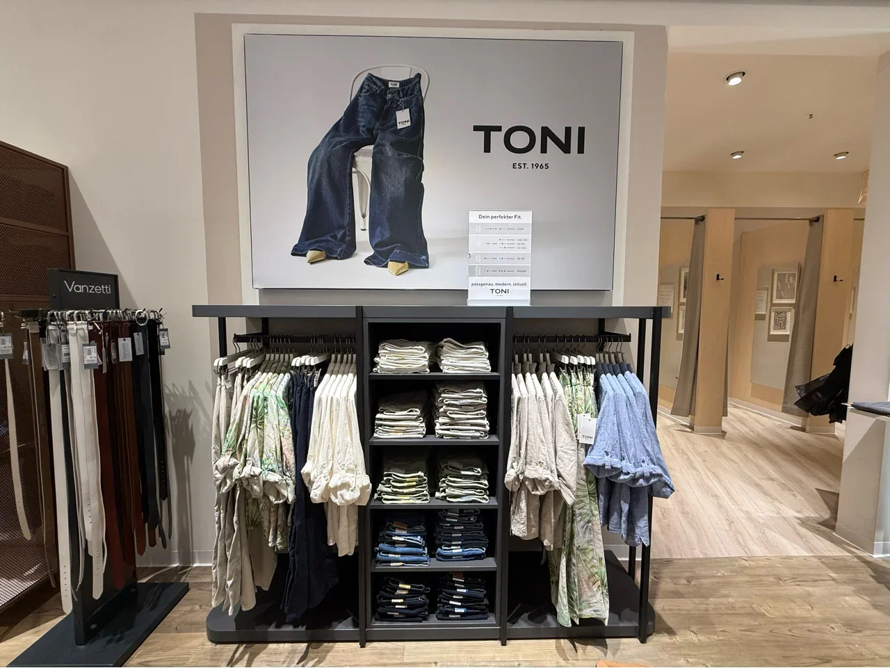 Display of folded pants and shirts in a clothing store, with a large billboard featuring jeans and the brand name 'TONI' above the display.