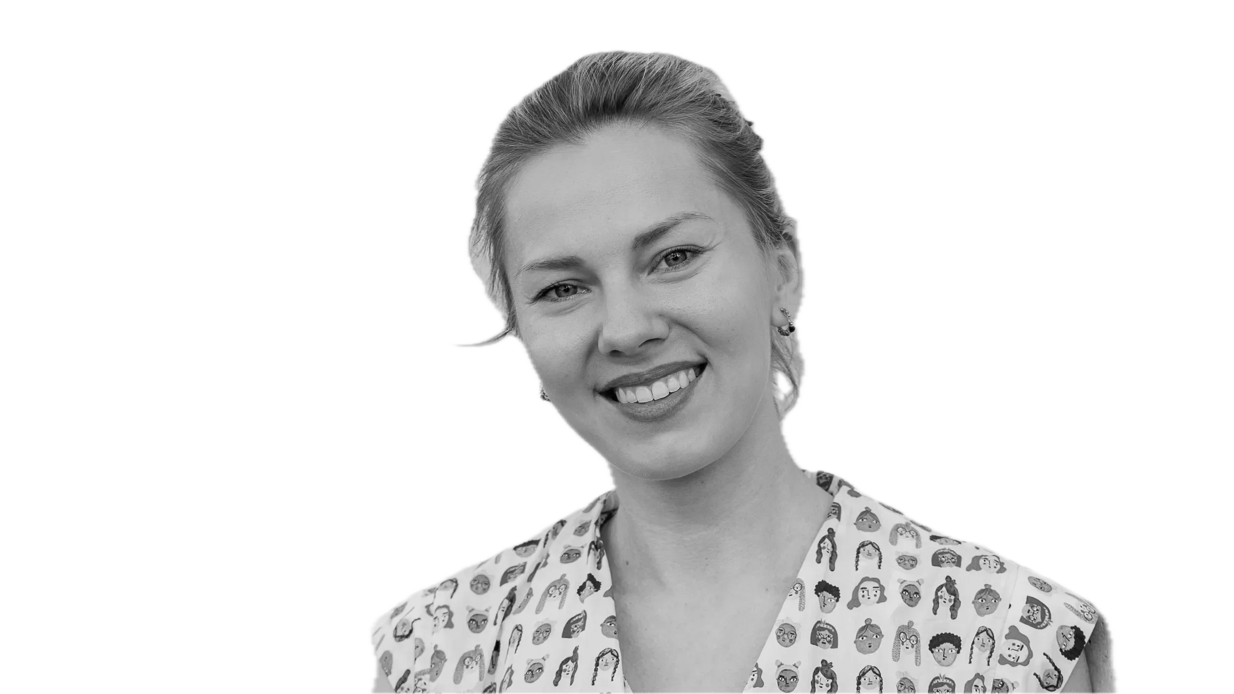 Black and white portrait of a smiling woman with light-colored hair tied back, wearing a shirt with cartoon face illustrations.