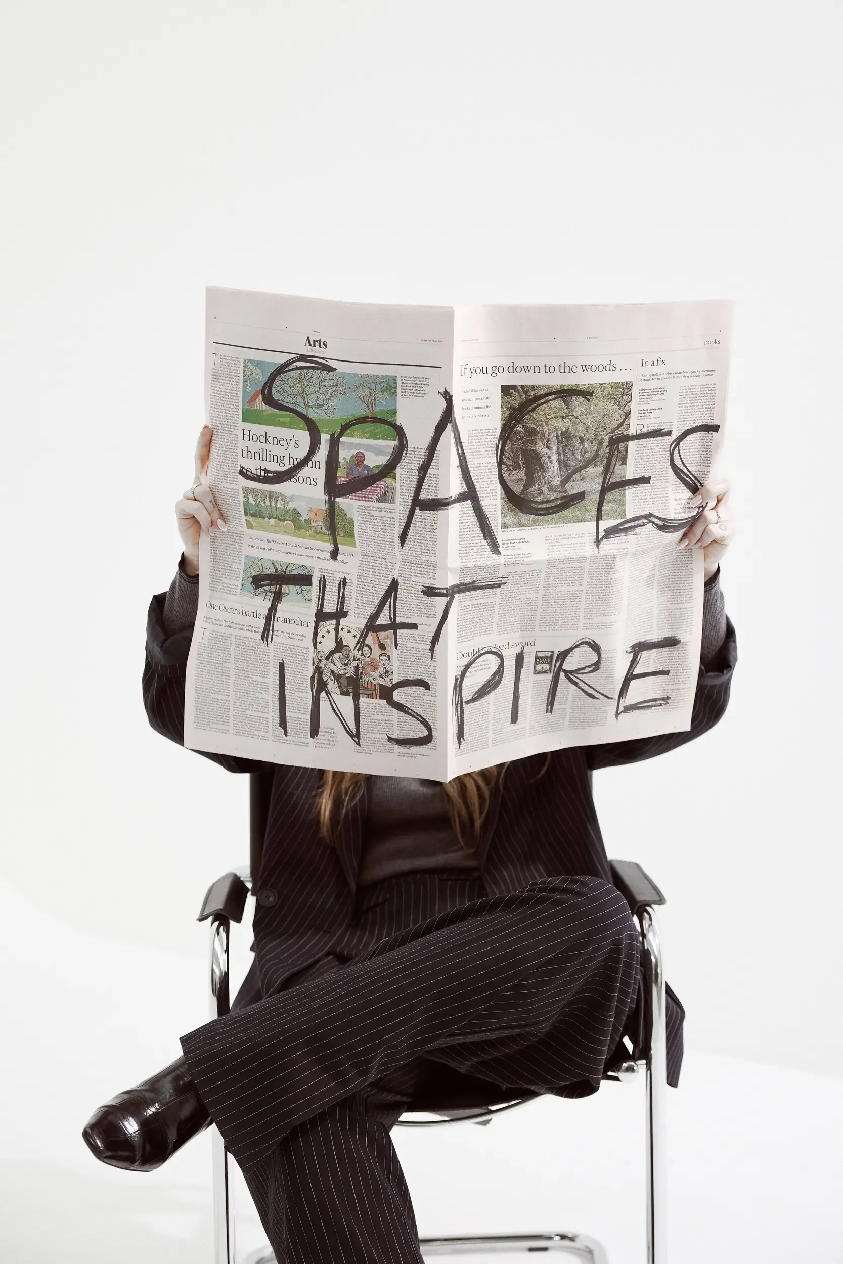 Person sitting on a chair holding a newspaper with the words "SPACE THAT INSPIRE" written on it.
