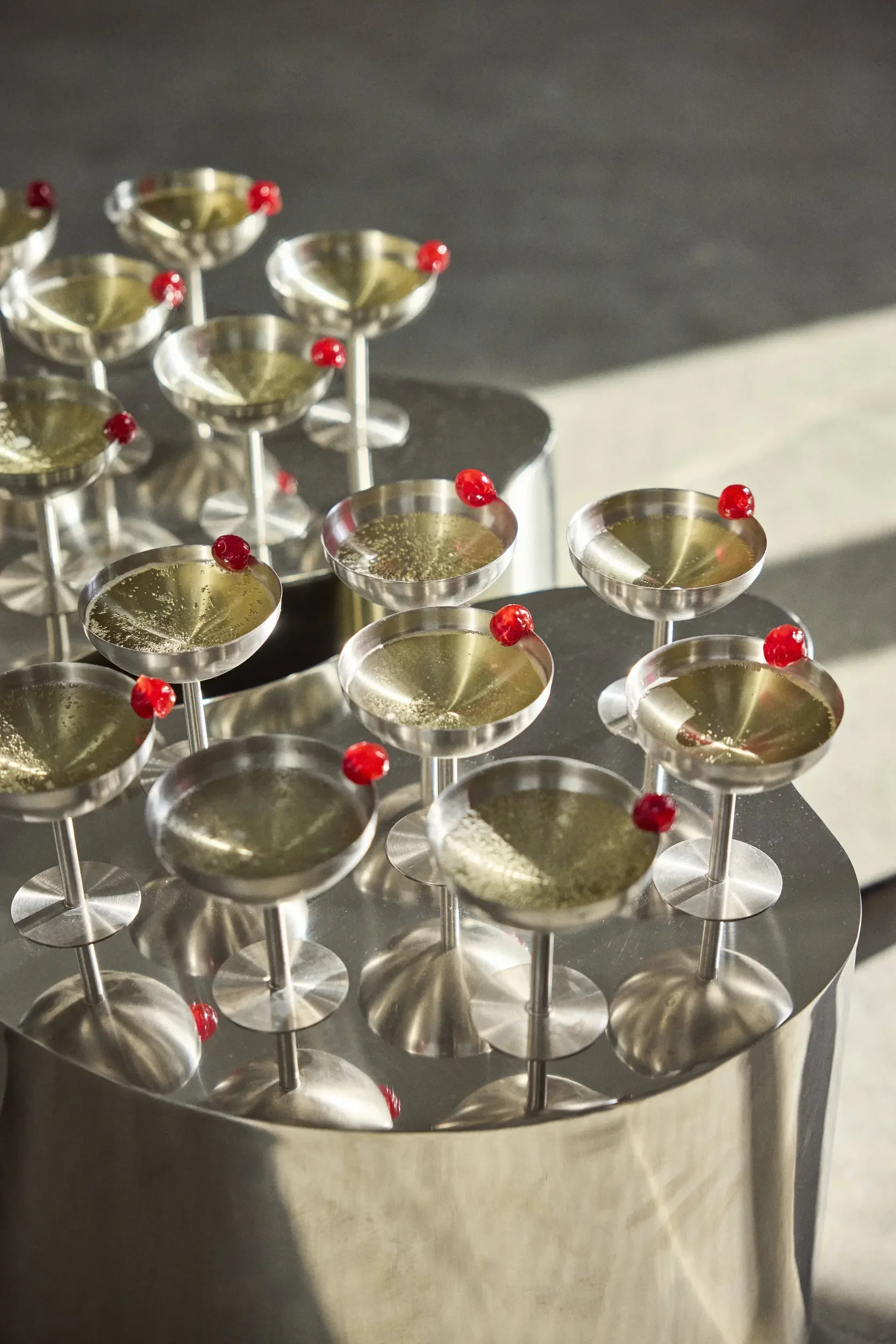 Multiple metallic cocktail glasses with red garnish on a shiny metallic table.