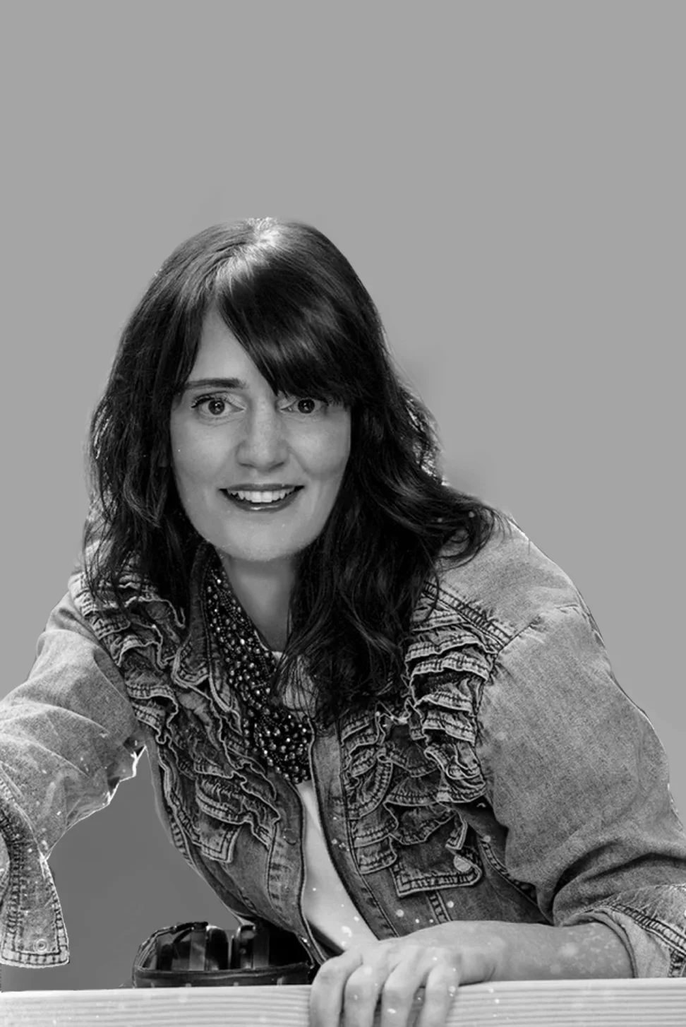 Black and white portrait of a woman with shoulder-length hair, smiling with visible teeth, in front of a black background.