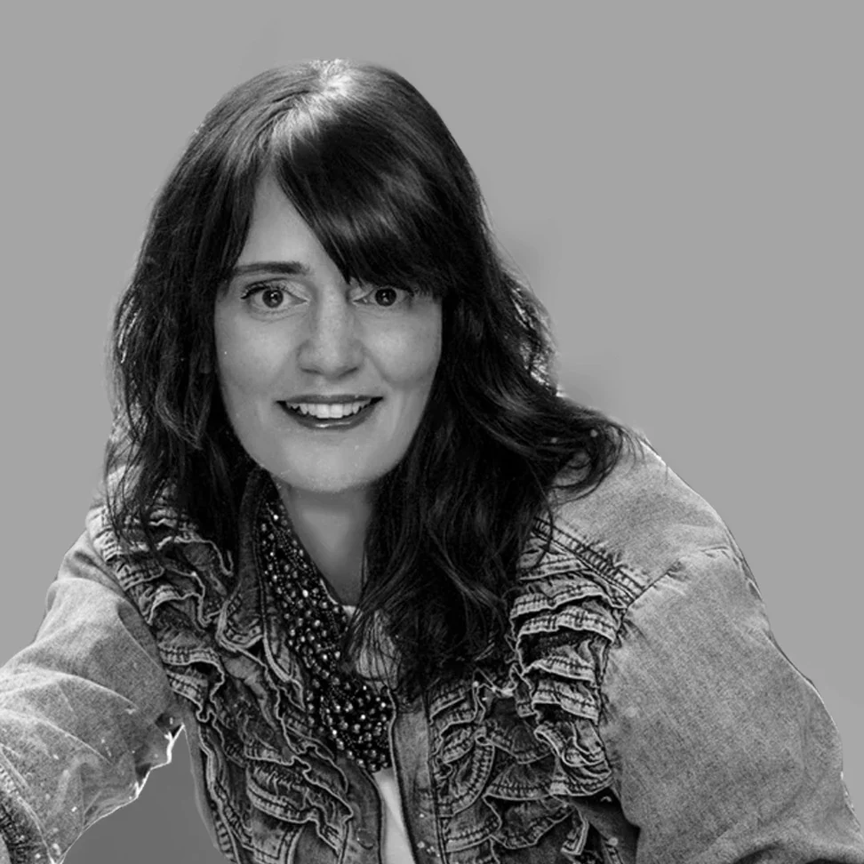 Black and white portrait of a woman with shoulder-length hair, smiling with visible teeth, in front of a black background.