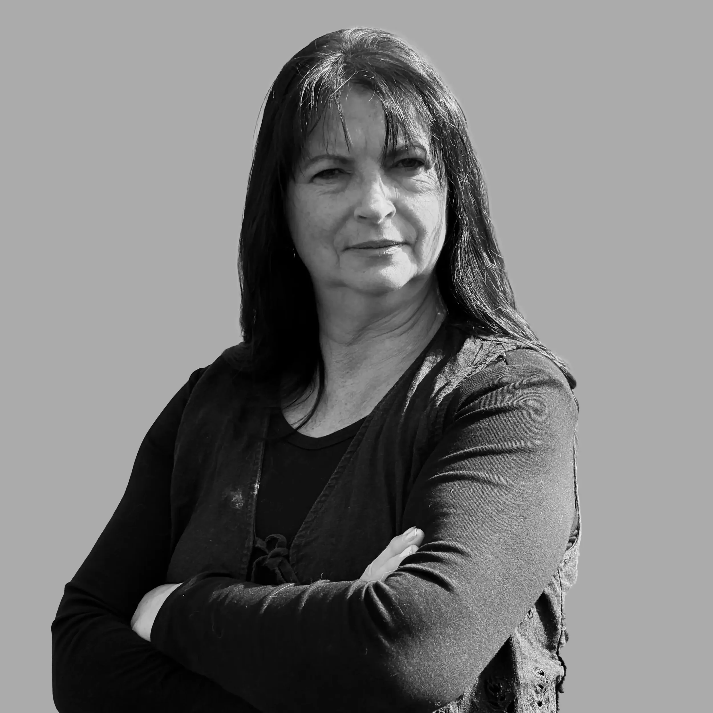 Black and white photo of a woman with long dark hair, crossed arms, looking confidently at the camera against a plain background.