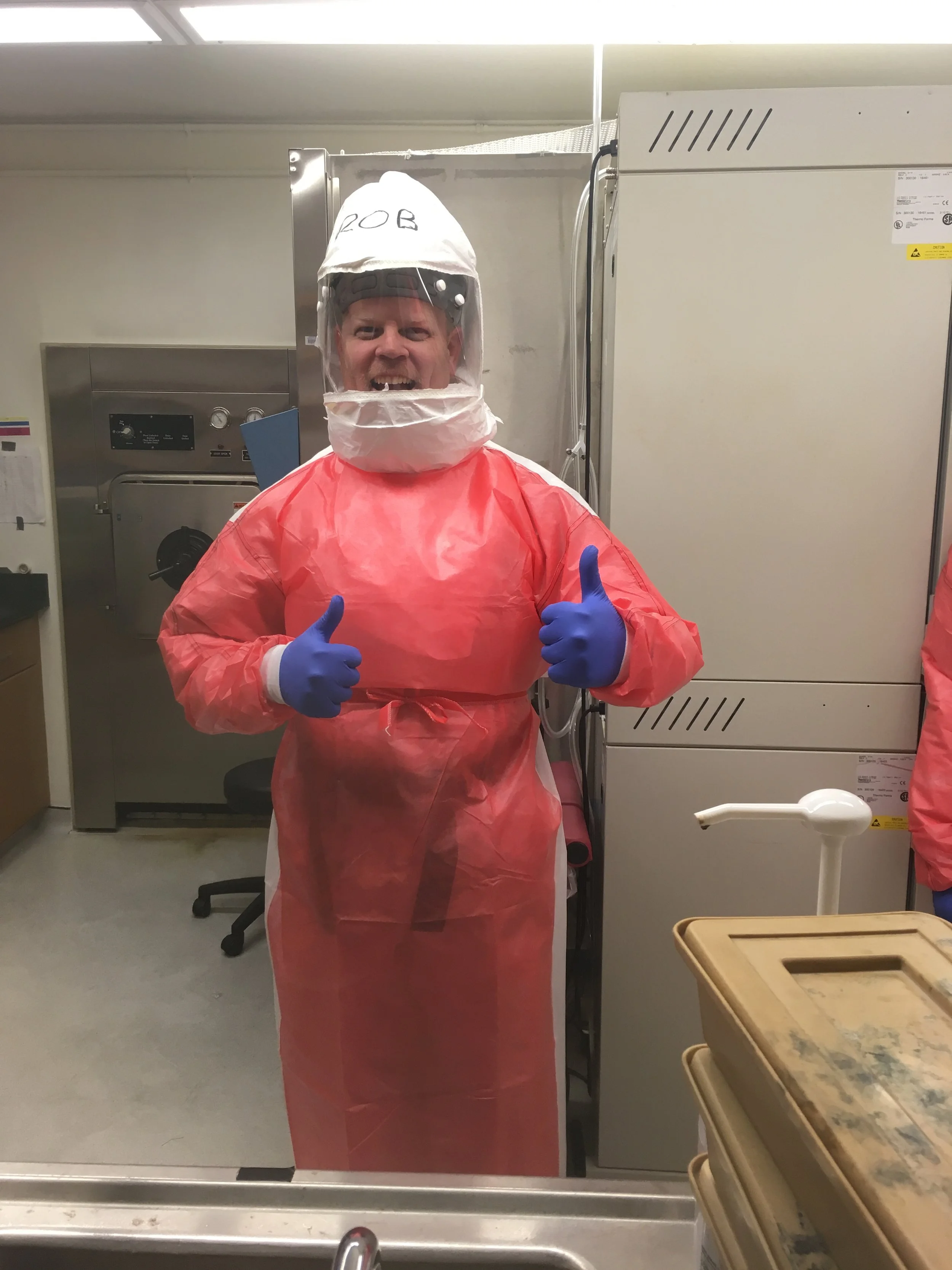 Person in a hazmat suit with a face shield, giving two thumbs up.