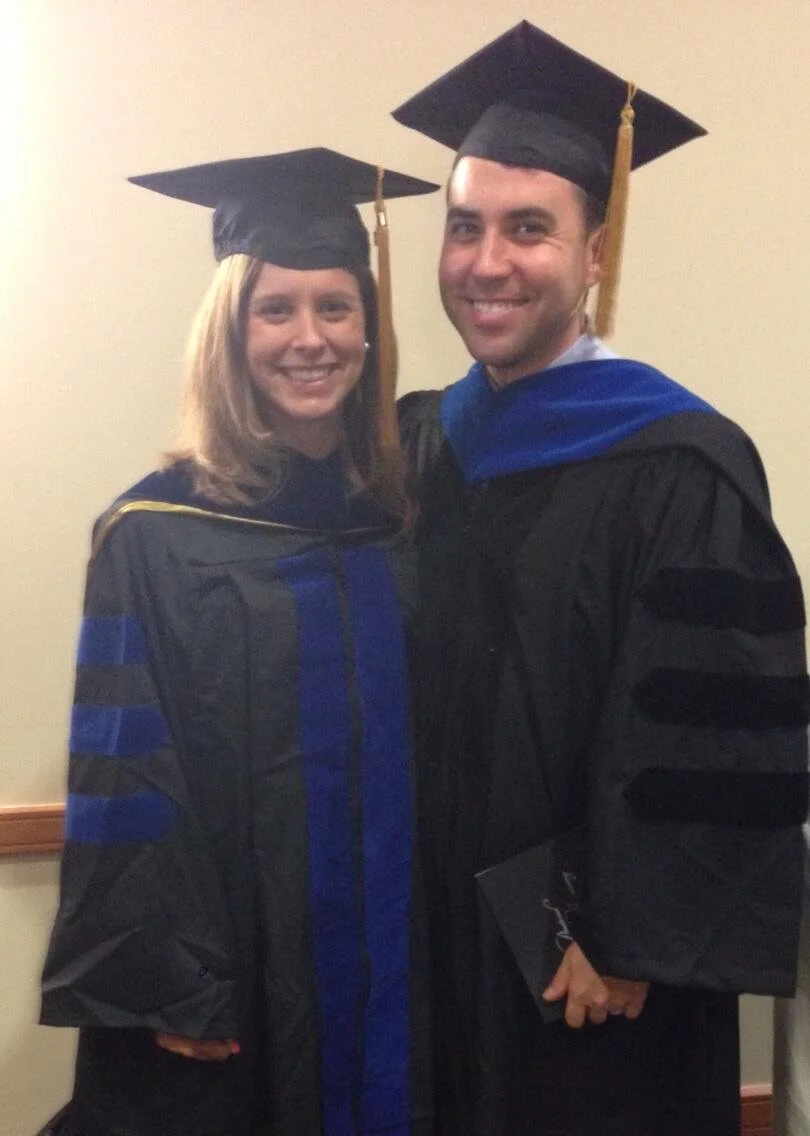 Two graduates wearing caps and gowns, smiling for a photo.
