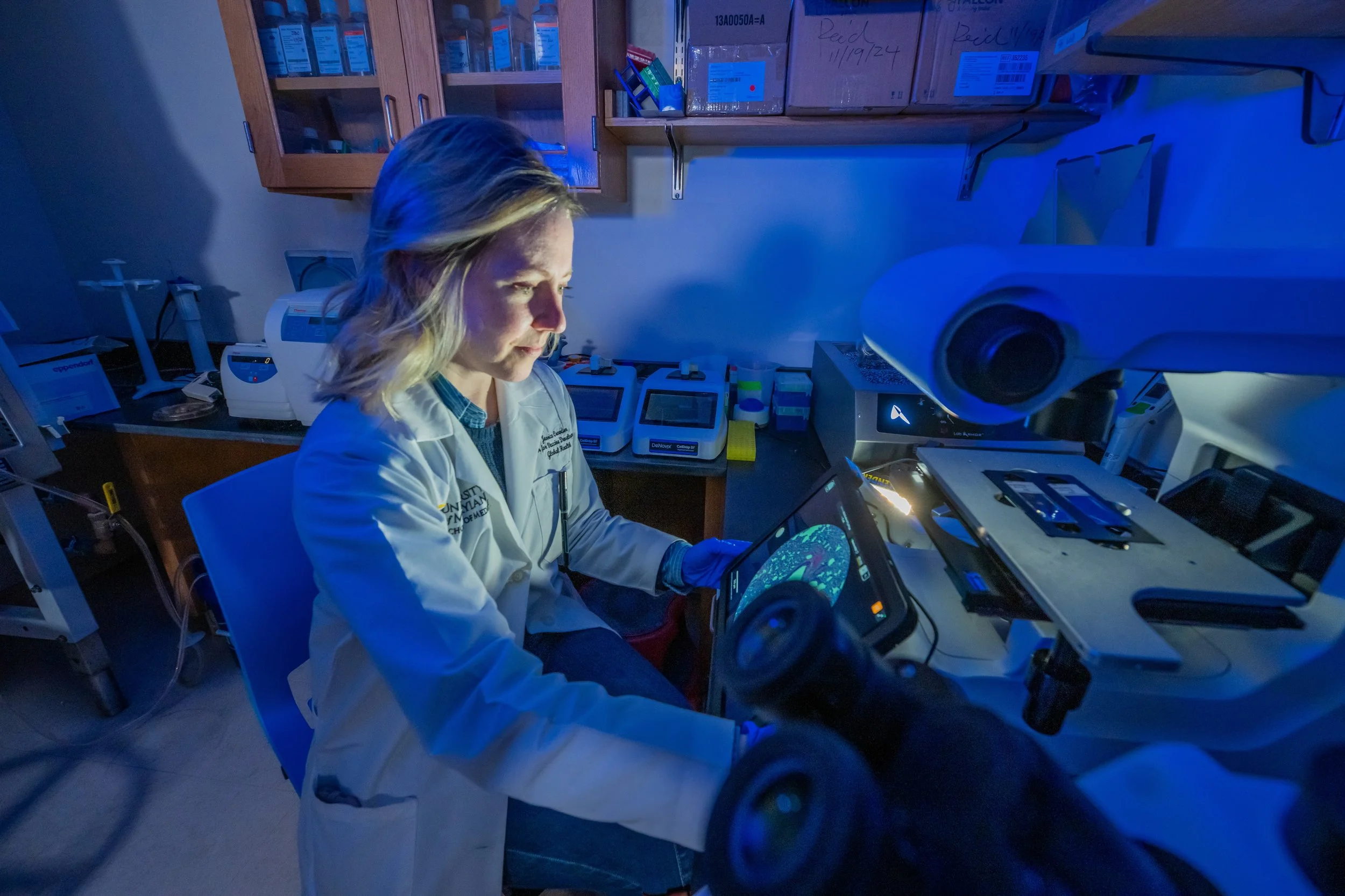 A scientist in a white lab coat working with microscopes and scientific equipment in a laboratory.